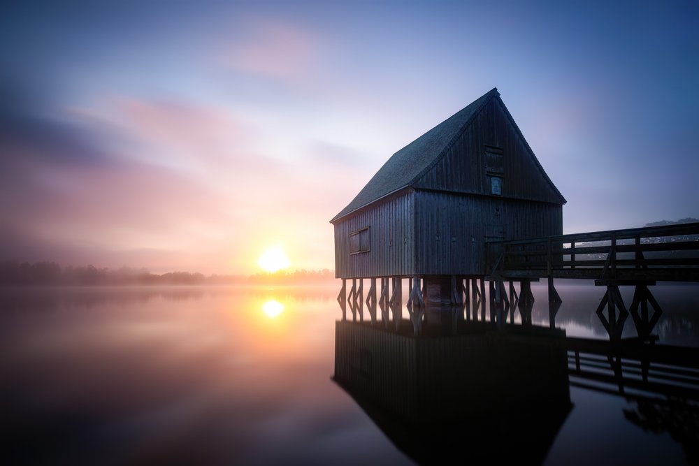 Nascer do sol na casa de barcos enevoada de Christoph Schaarschmidt