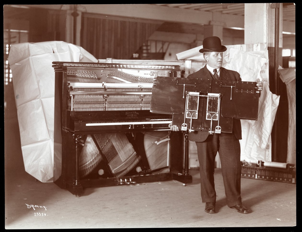 Um piano de Ricca und Son Piano Co. com um homem ao lado segurando parte das obras de piano, 1907 (impressão de gelatina de prata) de Byron Company