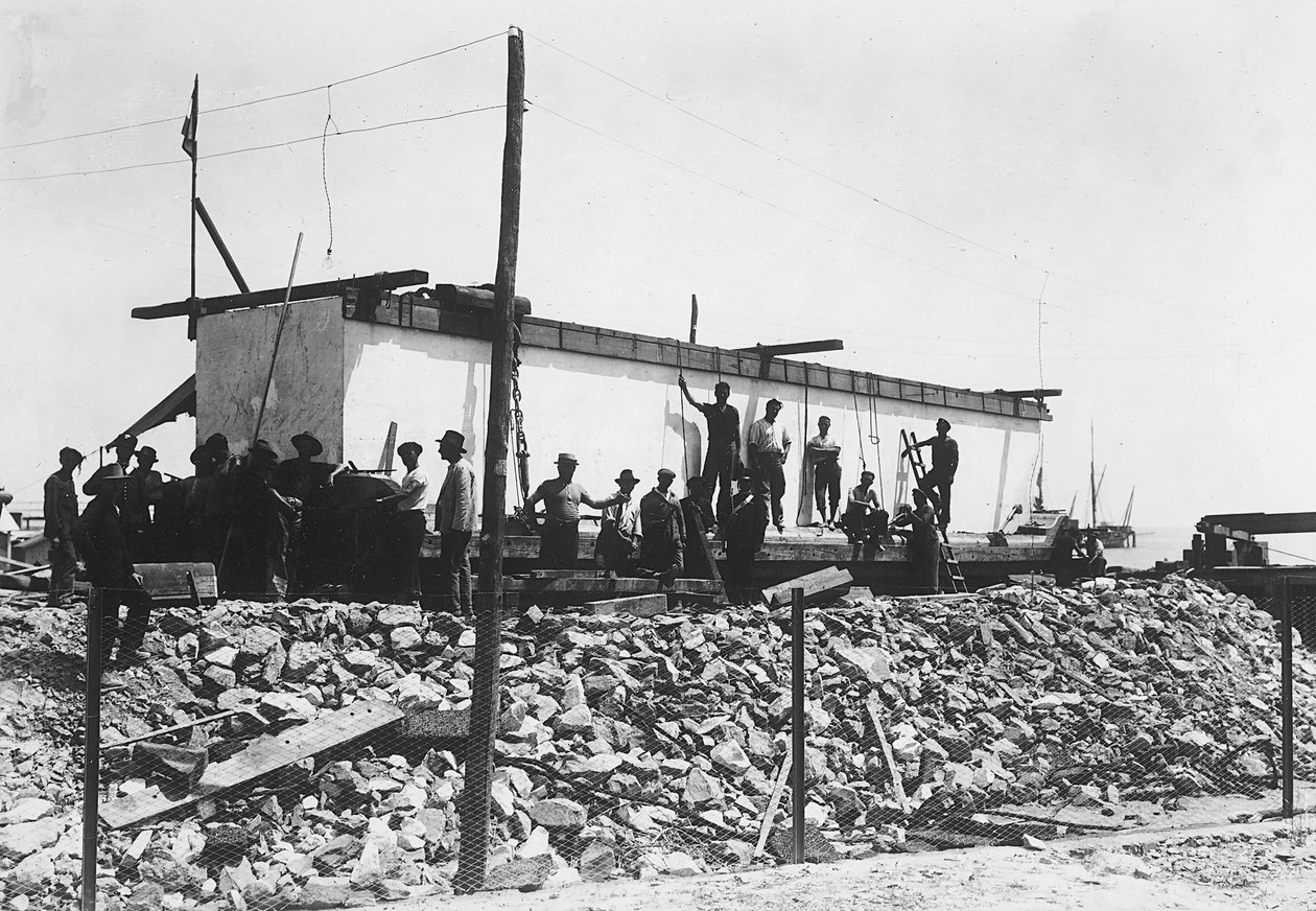 Vários homens ao redor de um enorme bloco de mármore já quadriculado, apenas transportados para o vale das pedreiras nos Alpes Apuanos (foto a p/b) de A. Corsini