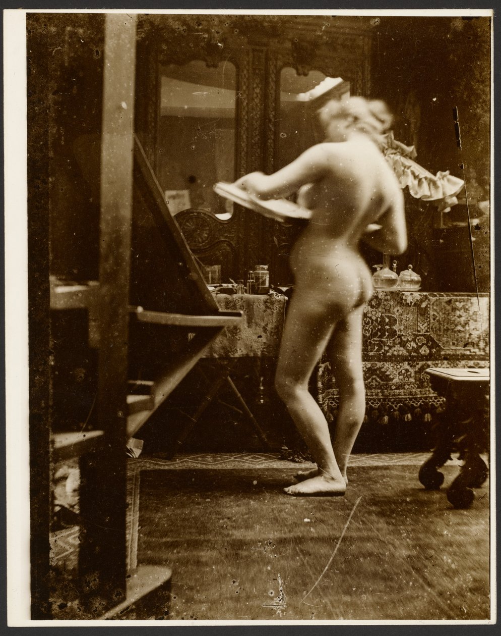 [Modelo de nu feminino em pé num estúdio com um caderno de esboços] de Alphonse Maria Mucha