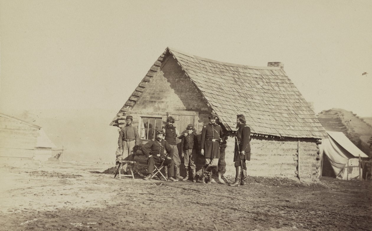 Um grupo de soldados e dois jovens, um afro-americano, estão fora dos aposentos da cabana de troncos, 1861-65. de American Photographer