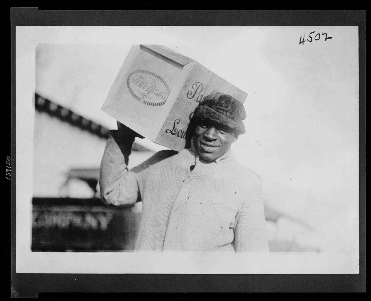 Homem afro-americano com uma caixa de uísque "Quatro Rosas" no ombro, possivelmente confiscado pelo Bureau de Receitas Internas dos EUA de American Photographer