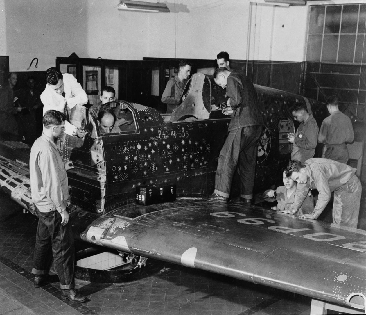 Os trainees soldados trabalham no "Flying Patch", um avião de combate Currtiss "Warhawk" sem montagem de motor ou cauda, com buracos de bala e remendos simulados, c.1942 de American Photographer