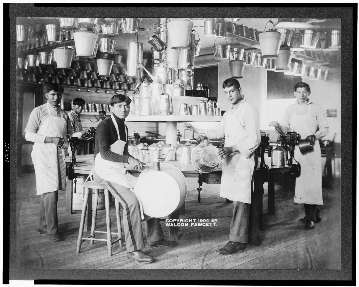 Jovens nativos americanos em oficina metalúrgica com baldes, lavatórios, regadores e outros artigos de metal, Carlisle Indian School, Pennsylvania, c.1904 (foto a p/b) de American Photographer