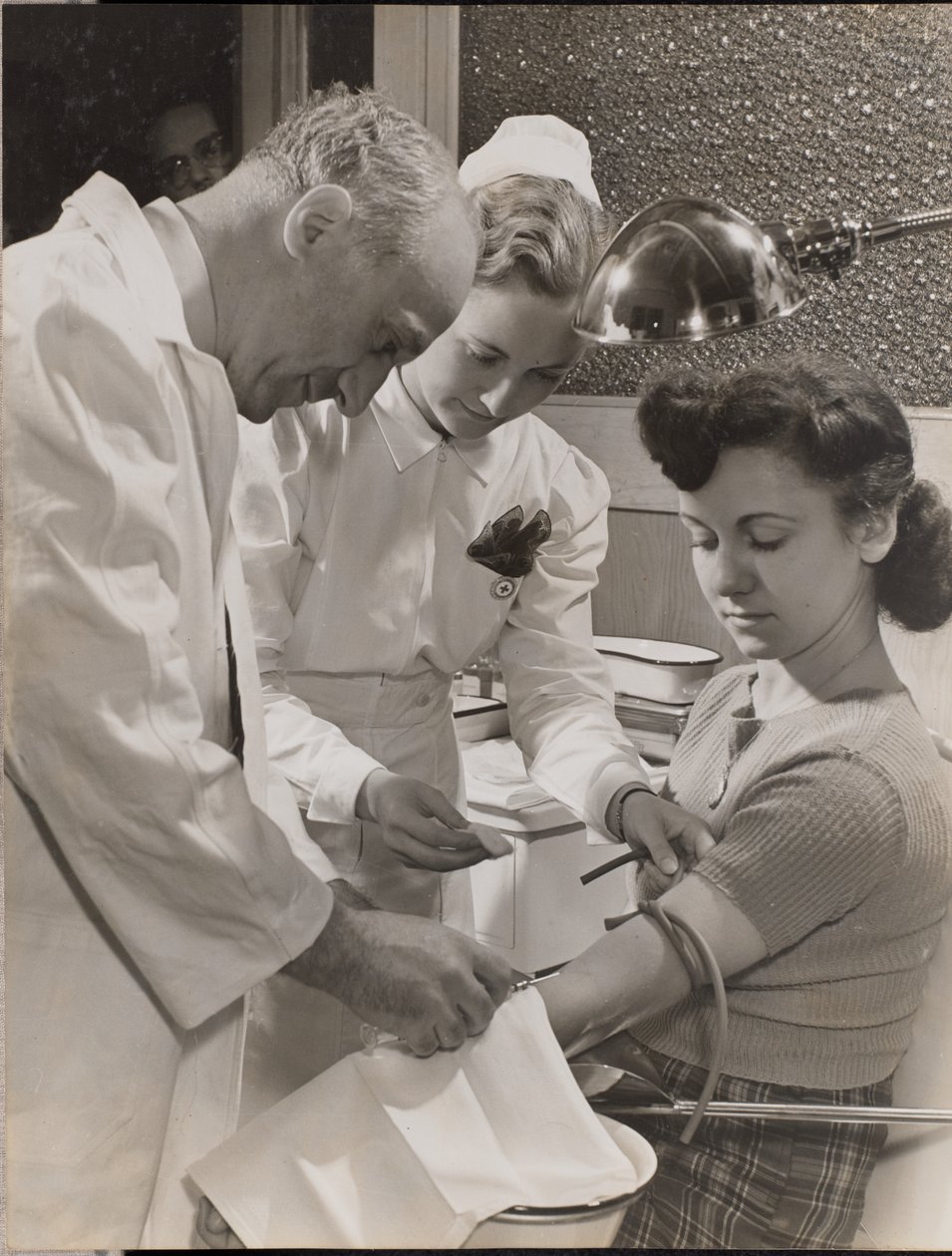 [Médico e enfermeira introduzem uma agulha no braço de uma mulher]. de Arnold Eagle