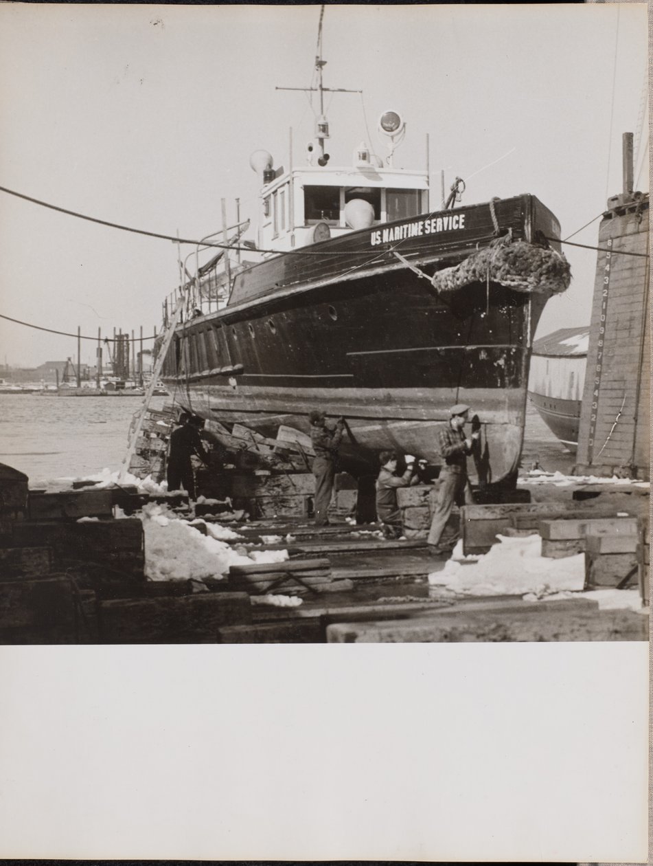 [Quatro homens reparam a parte inferior de um barco ancorado] de Arnold Eagle