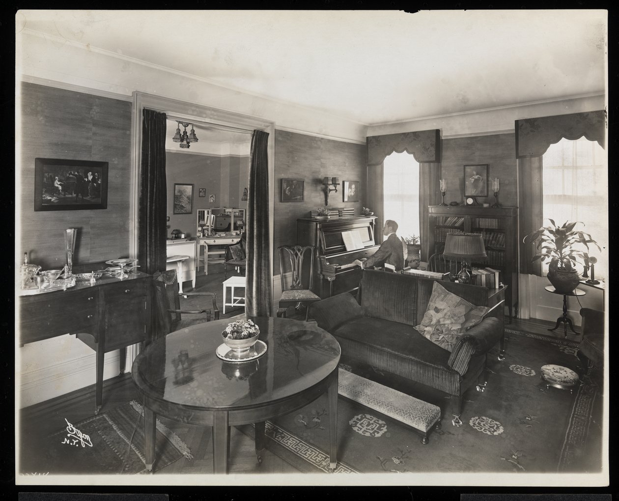 Um homem tocando piano em uma sala de estar da residência AC Cronin, 1915-16 (impressão em gelatina de prata) de Byron Company