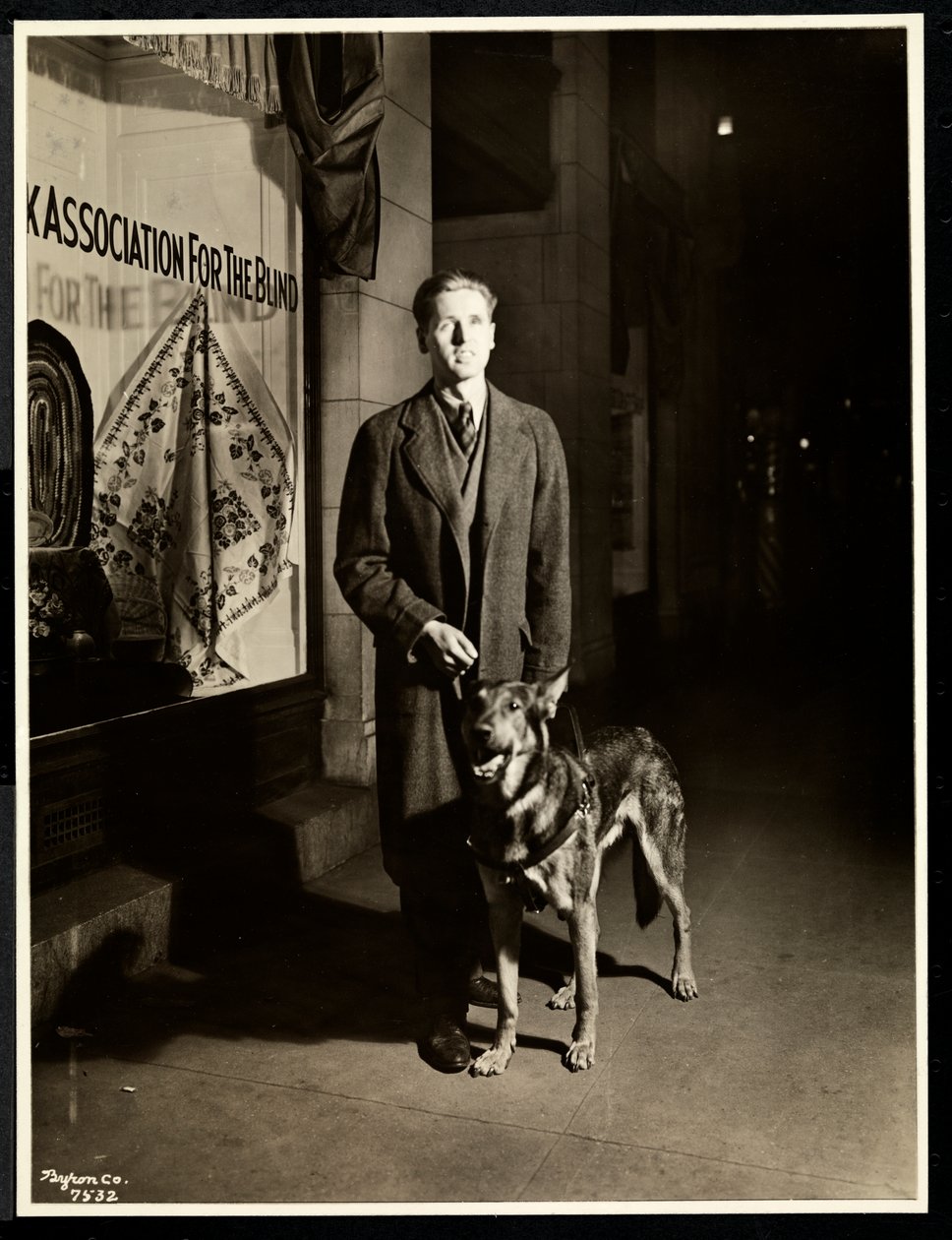 Homem cego e seu cão-guia na calçada em frente à Associação Nova York para os Cegos, 111 East 59th Street, Nova York, 1938 (impressão em gelatina de prata) de Byron Company