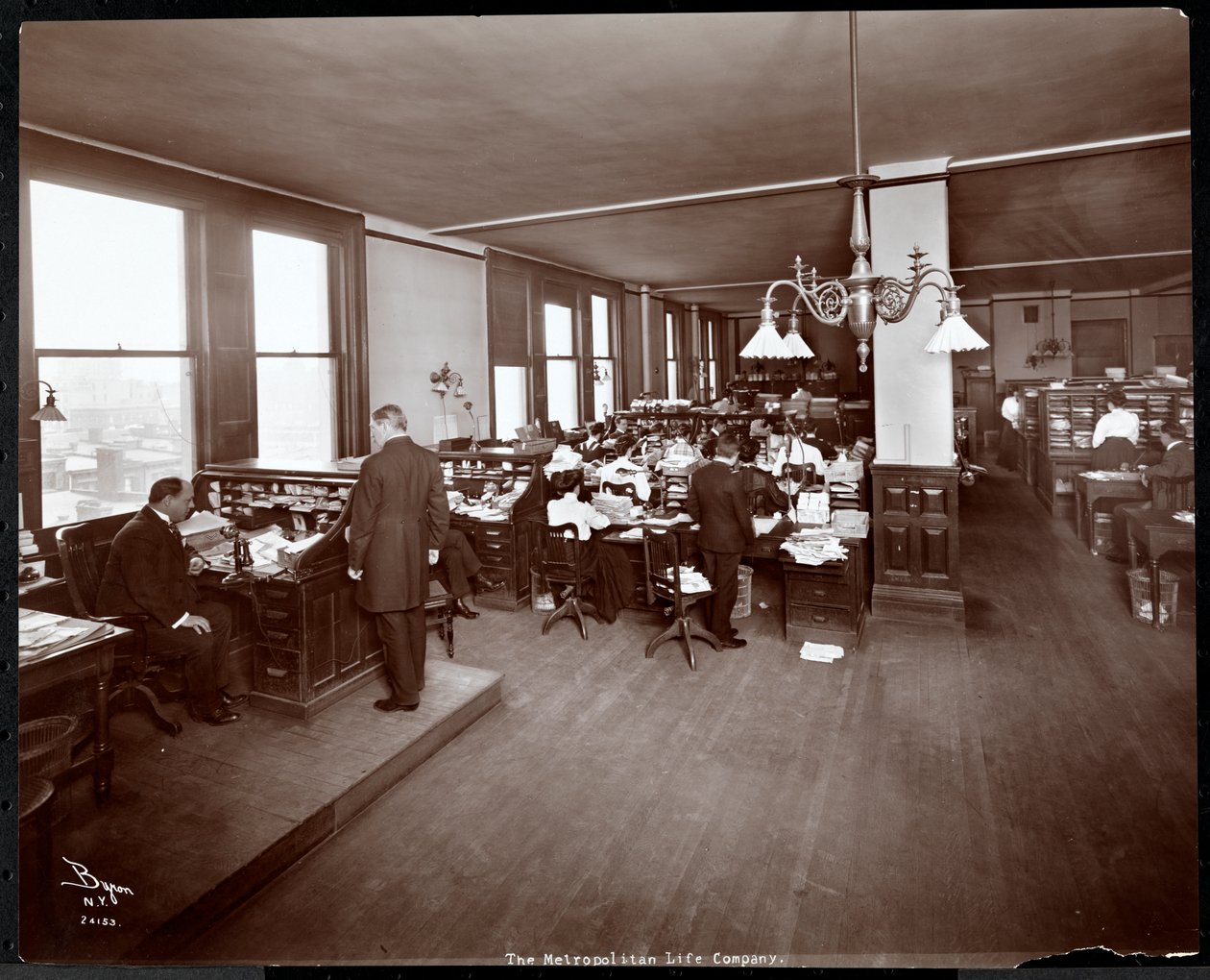 Homens e mulheres trabalhando em mesas em um escritório na Metropolitan Life Insurance Co. na 23rd Street e Madison Avenue, Nova York, 1907 (impressão em gelatina de prata) de Byron Company