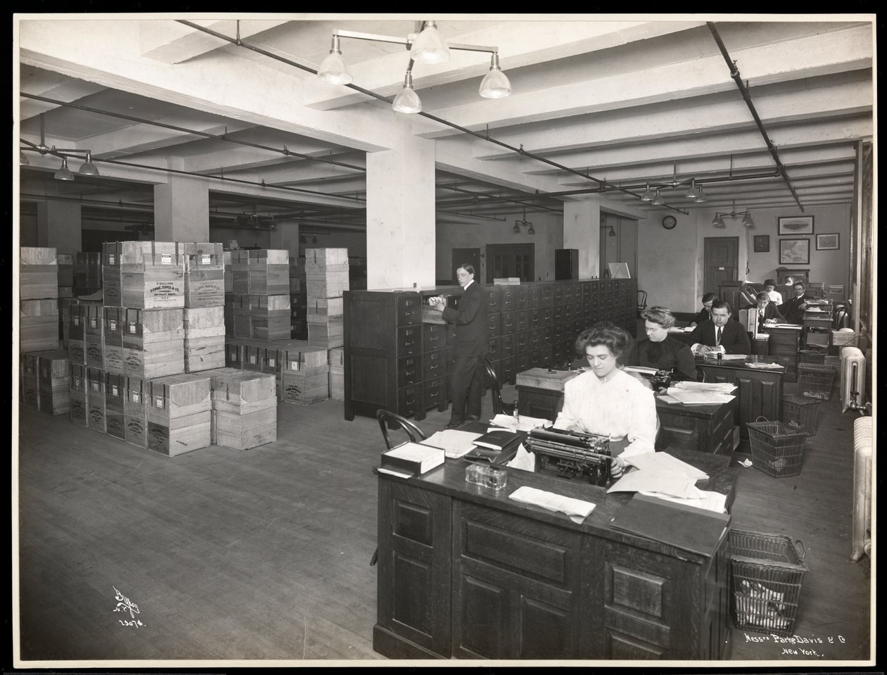 Visão de homens e mulheres em mesas no que parece ser uma sala de expedição em Parke, Davis und Co., químicos, Hudson und Vestry Streets, Nova York, 1910 (impressão em gelatina de prata) de Byron Company