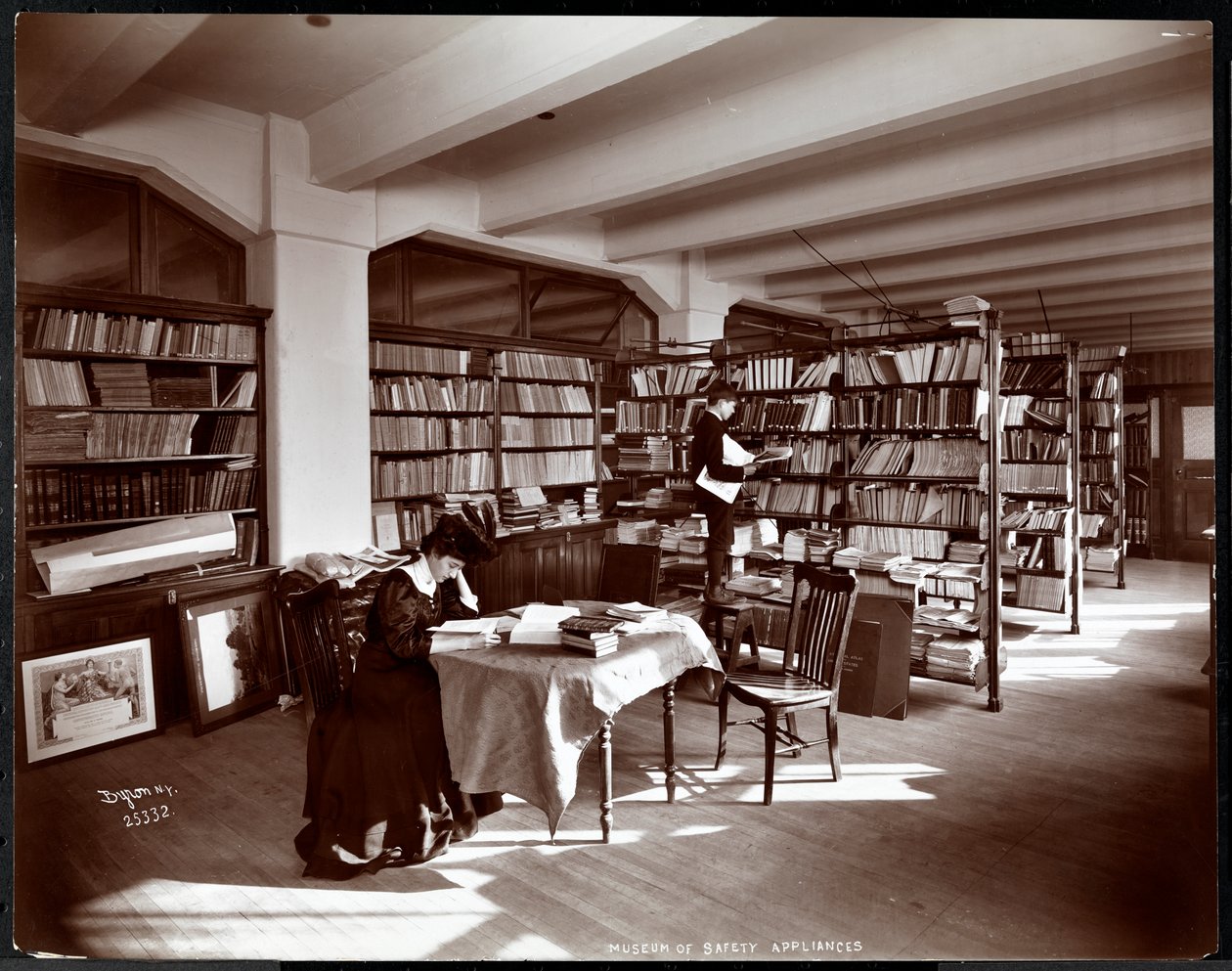 Mulher e um jovem em uma biblioteca do Museu de Dispositivos de Segurança do Instituto Americano de Serviço Social, Nova Iorque, 1907 (impressão de gelatina de prata) de Byron Company