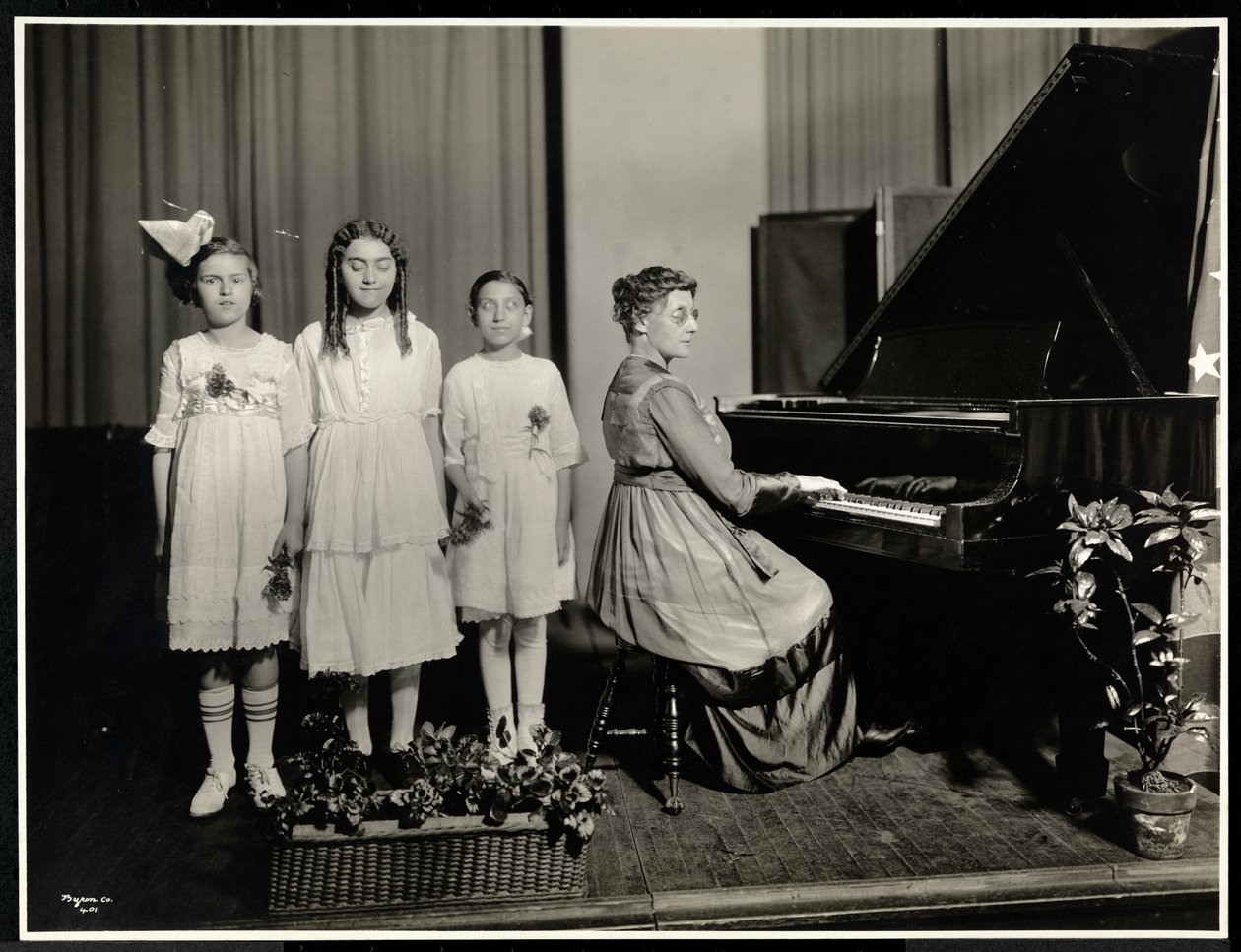 Mulher tocando piano enquanto três garotas cantam na Associação Nova York para os Cegos, 111 East 59th Street, Nova York, c.1917 (impressão em gelatina prateada) de Byron Company