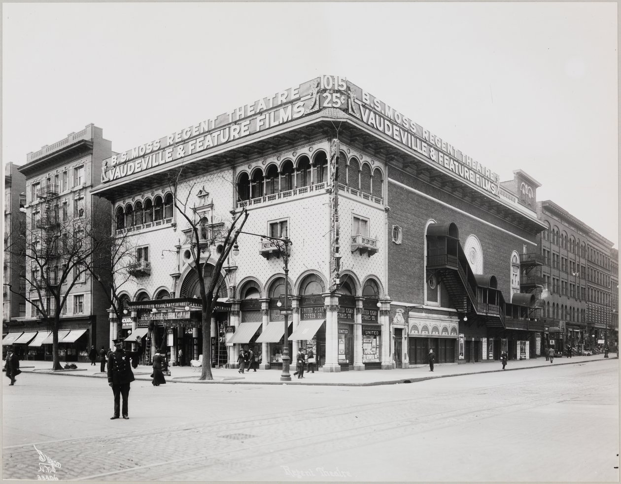 Um teatro enorme com uma fachada elaborada, completo com arcos e varandas mouriscas. Uma grande placa no topo do edifício diz "B.S. Moss Regent Theatre Vaudeville & Feature Films". Uma placa publicitária de Olga Petrova em "O Coração de uma Mulher Pintada" de Company Byron
