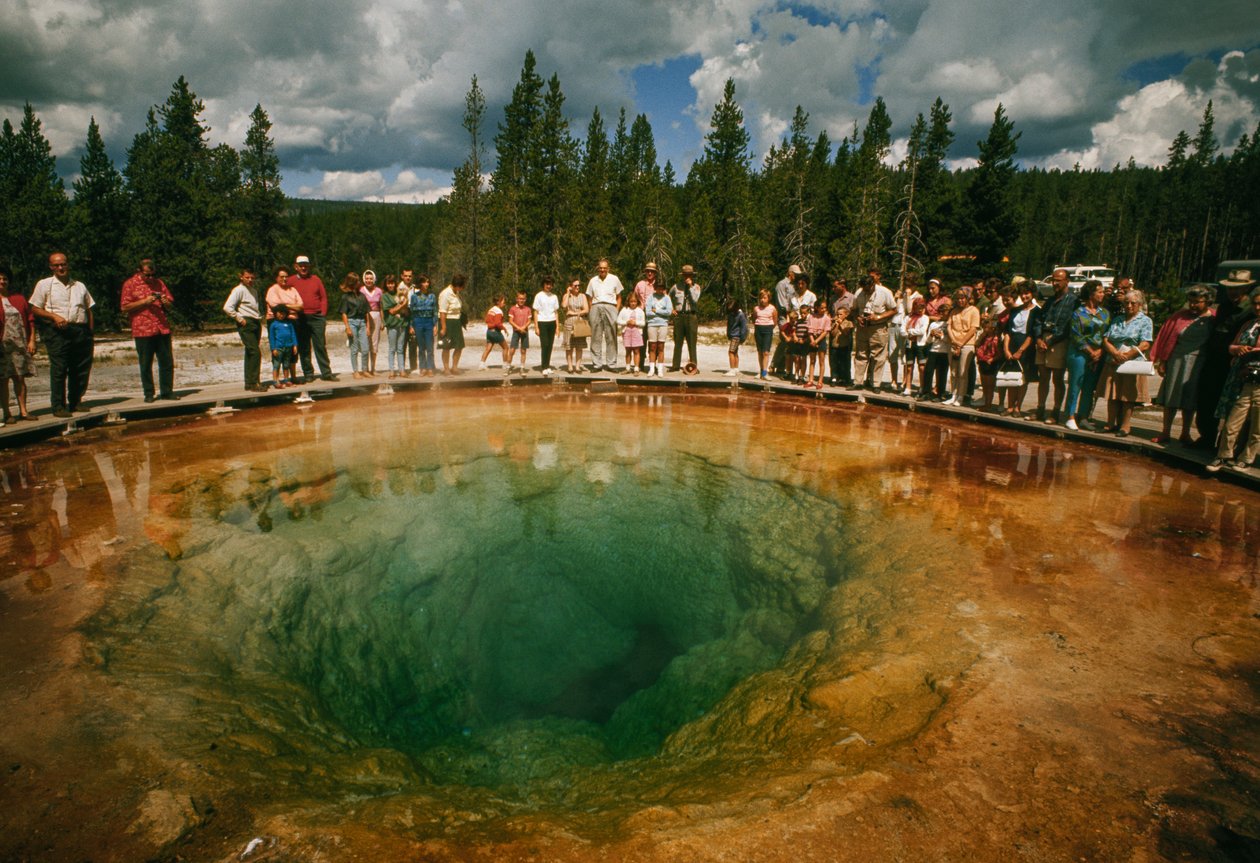 Os visitantes do parque reúnem-se à volta de uma piscina termal azul-esverdeada em forma de flor. O Parque Nacional de Yellowstone... de Dean Conger
