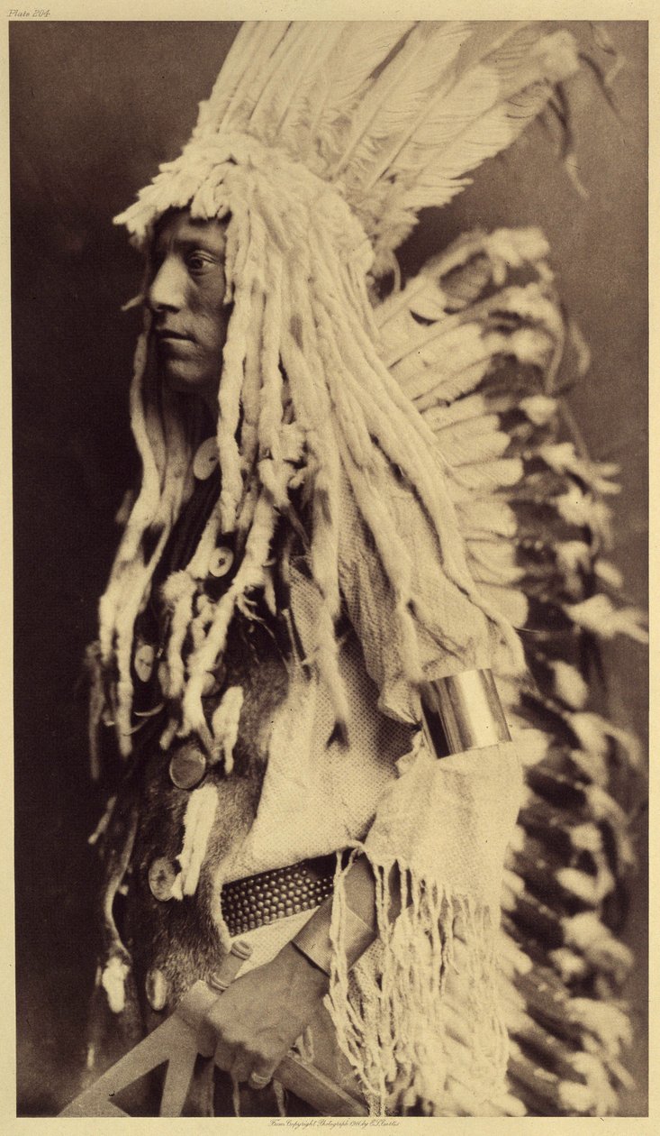 Pessoa idosa, Piegan. Os jovens não perdem nenhuma ocasião de festas públicas para vestirem as roupas do seu pai guerreiro. Foto tirada do volume 6 da enciclopédia publicada por Edward S. Curtis (1868-1952) sobre os índios da América do Norte, com um desta de Edward Sheriff Curtis