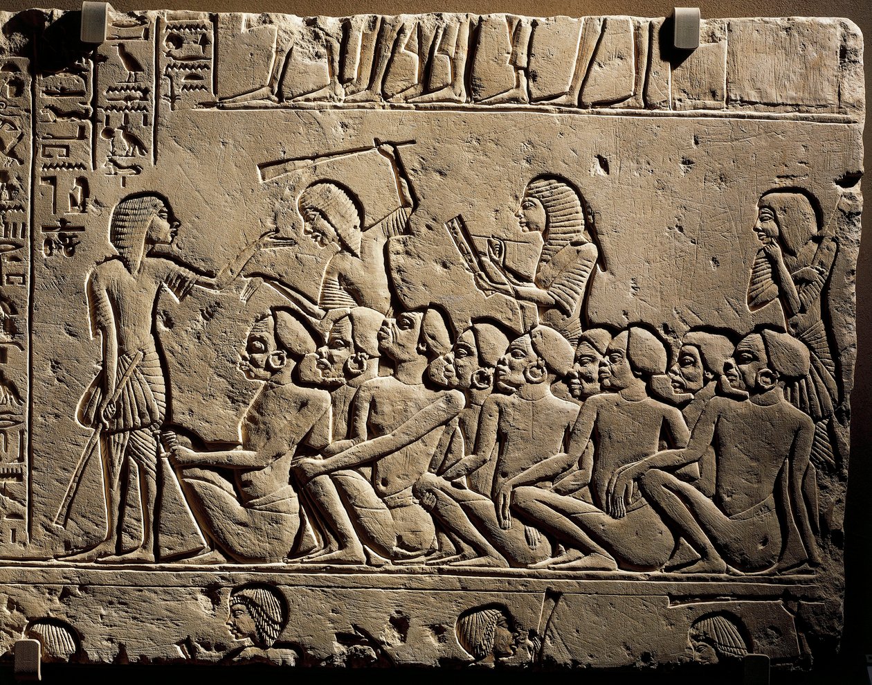 Um grupo de prisioneiros negróides rodeados por guardas armados com bastões enquanto um escriba redige um relatório, relevo do túmulo de Horemheb em Saqqara de Egyptian 18th Dynasty