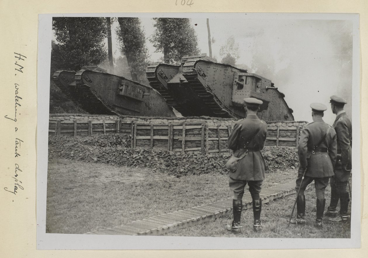 Três oficiais, um deles possivelmente o rei George V, observando dois tanques sendo conduzidos sobre um obstáculo, 1915-1918 de English Photographer