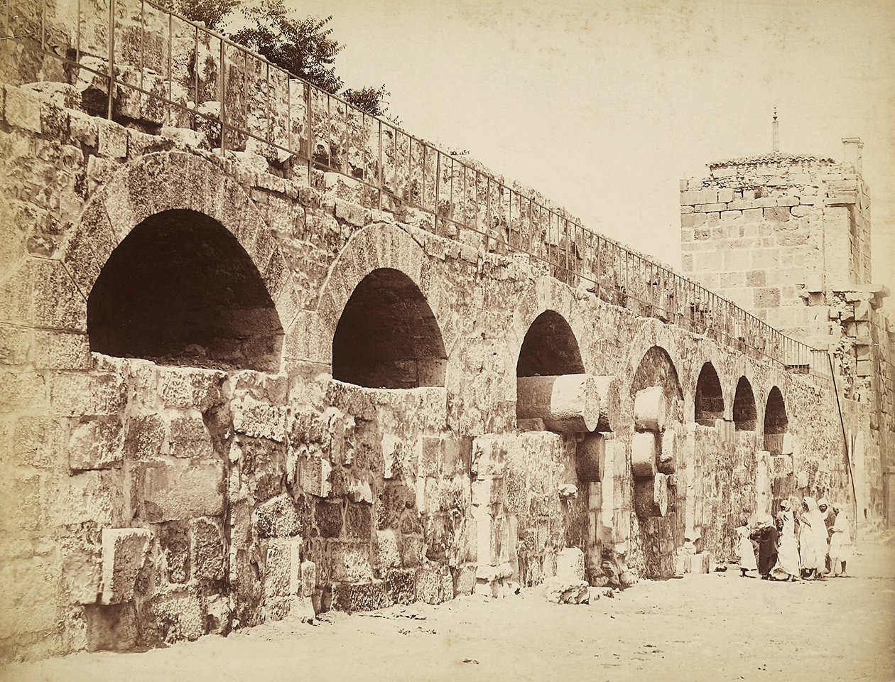 Vista das muralhas da cidade de Heliópolis ou Baalbek, antiga cidade síria, agora Líbano. Um grupo de pessoas está reunido perto da muralha. de Félix Bonfils
