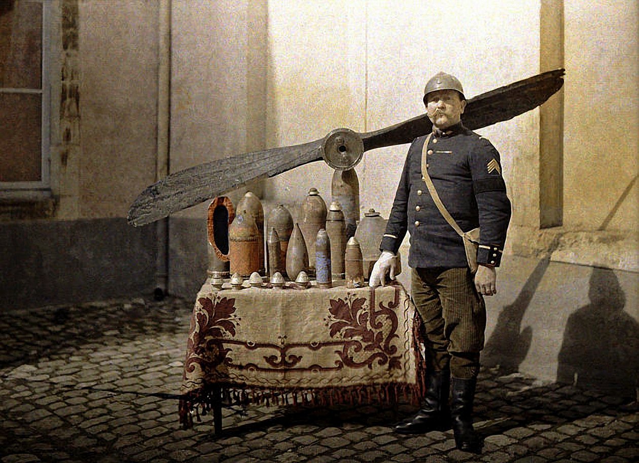 Um soldado francês ao lado de uma mesa com granadas alemãs e uma hélice de avião, Reims, Marne, 1917 (autocrômico) de Fernand Cuville