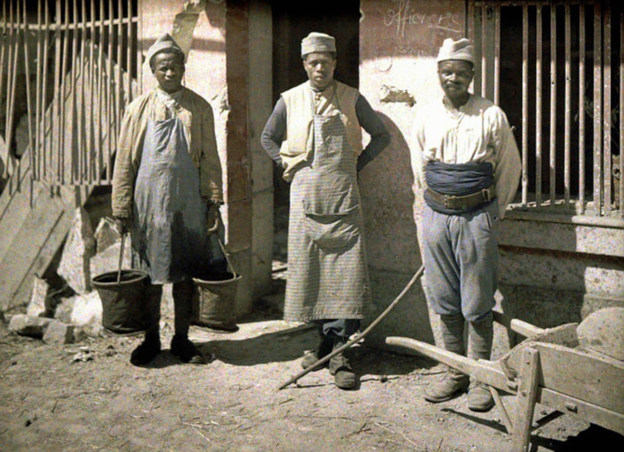 Três trabalhadores do Senegal em frente a uma casa, Soissons, Aisne, França, 1917 (autocrômico) de Fernand Cuville