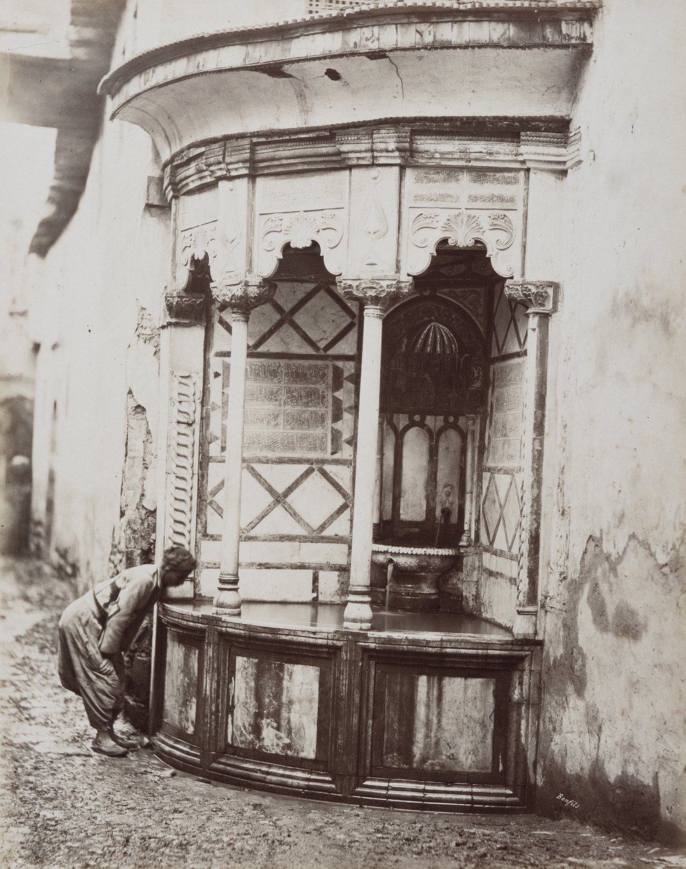 Um homem a beber de uma fonte da esquina, numa rua de Damasco, na Síria. de Félix Bonfils