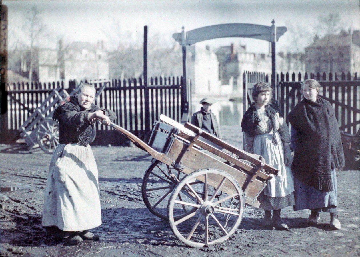 Mulher velha com um carrinho em uma estrada lamacenta, com duas meninas e um menino, França, c.1914-18 (autocrômico) de French Photographer