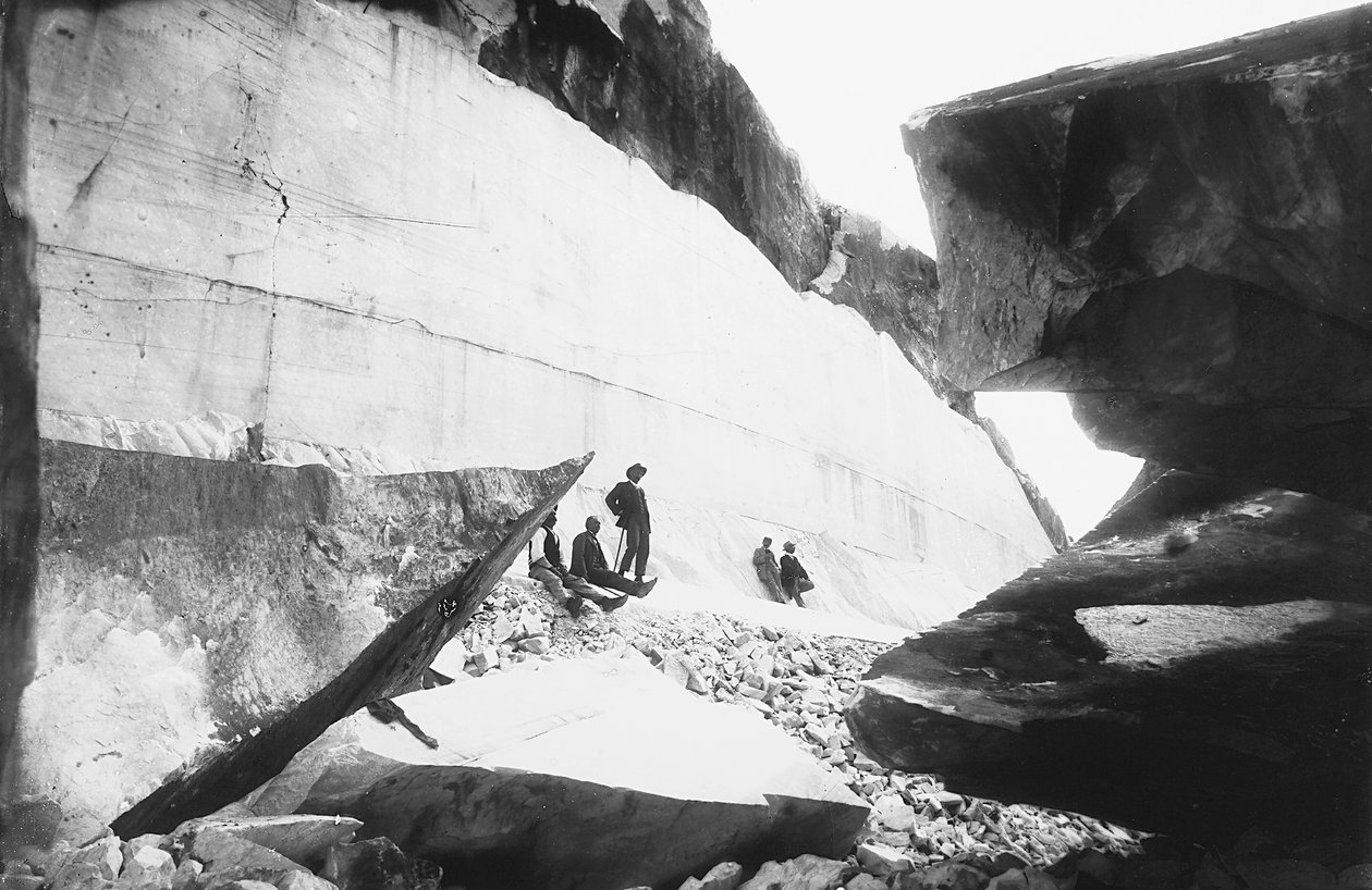 Alguns homens sentados ao longo das paredes de uma pedreira de mármore, nos Alpes Apuanos (foto a p/b) de G. Armani