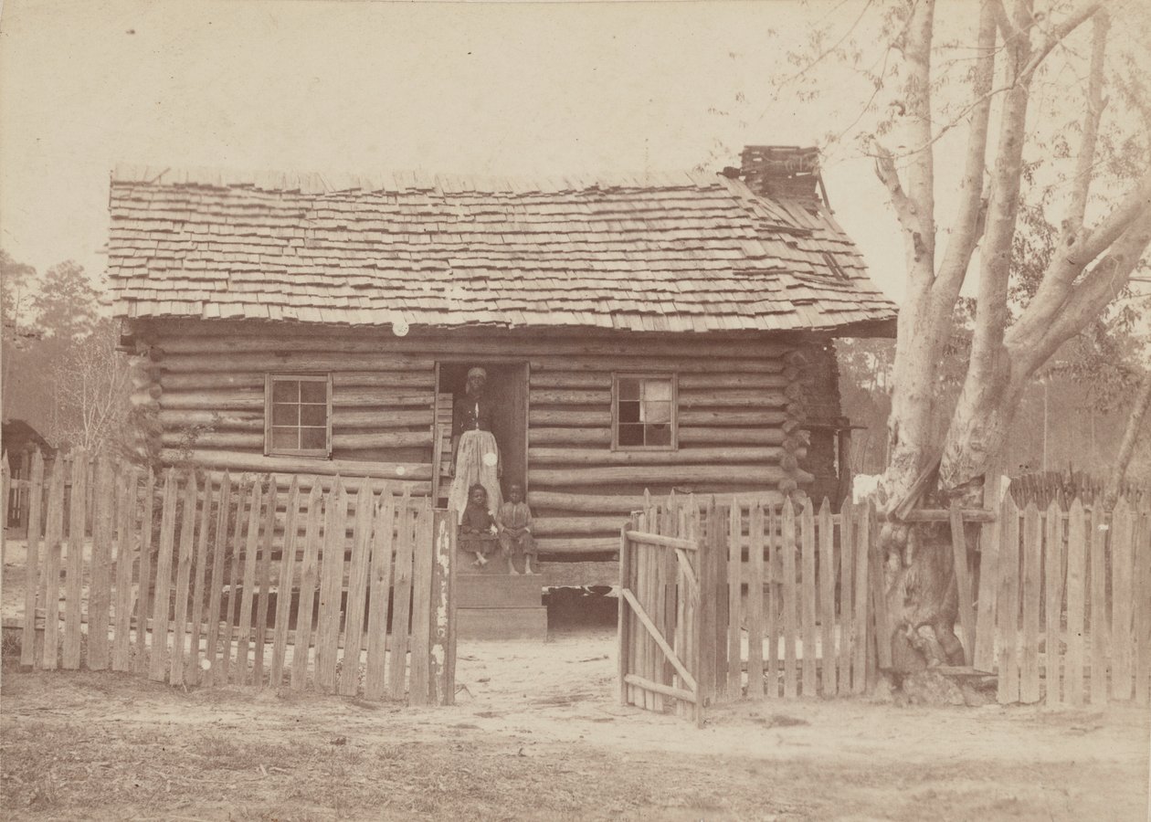 Impressão de albumina de uma mulher e duas crianças em frente a uma casa de toras na Geórgia, década de 1880. de H. S. Clark