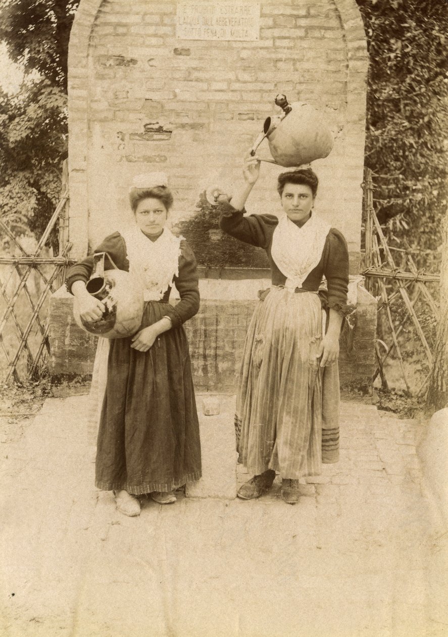 Duas jovens mulheres vestindo roupas tradicionais e carregando jarros de terracota perto de um poço, Marche, Itália, cerca de 1910 de Italian Photographer