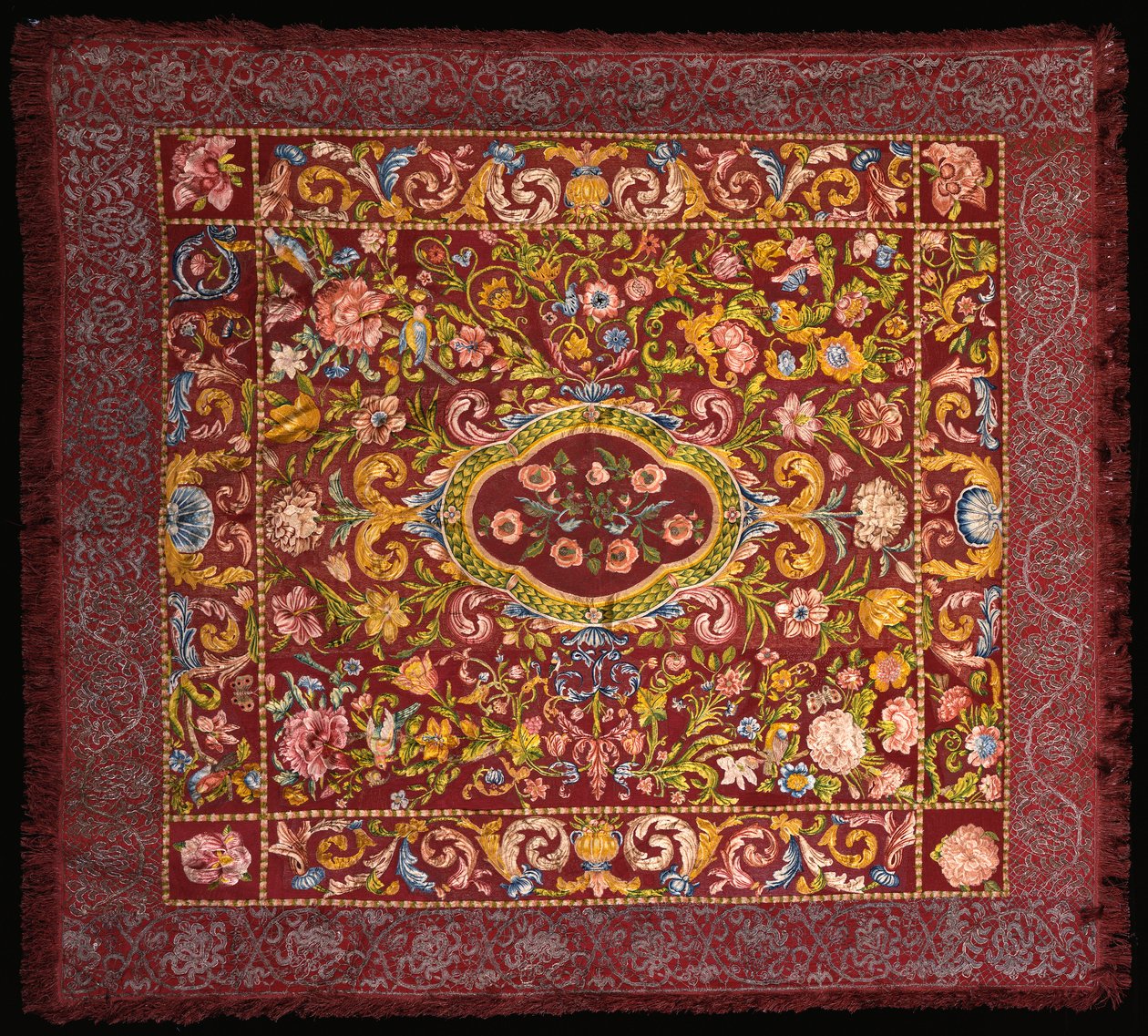 Um tapete de mesa italiano bordado em sedas de cores vivas com um medalhão central de rosas em um campo de lírios e flores maiores de Italian School