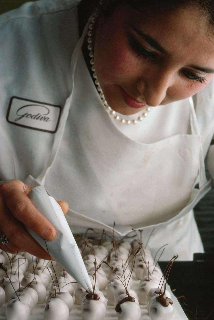 Um chefe de cozinha da Godiva coloca hastes de chocolate em cerejas cobertas de fondant. Bruxelas, Bélgica. de James L Stanfield