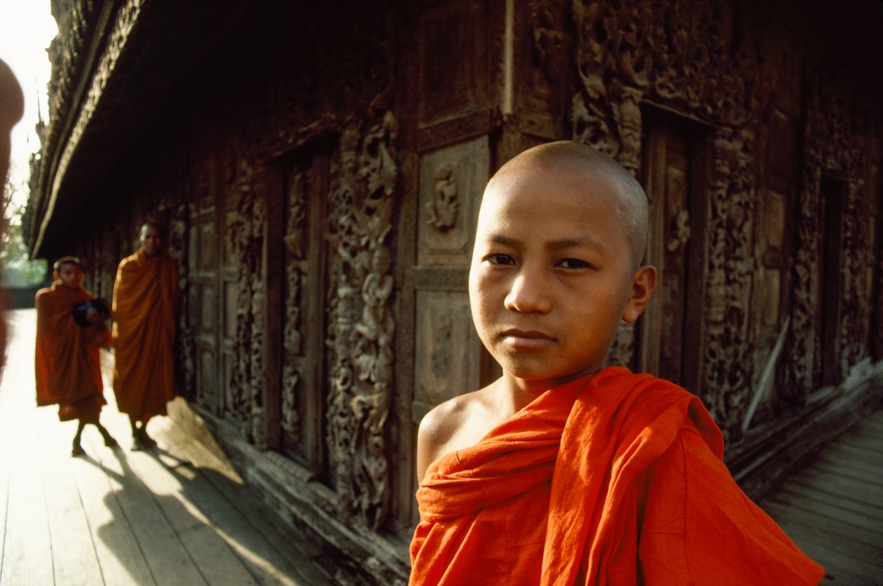 Um jovem monge noviço em frente a painéis de teca esculpidos. Mosteiro de Shwenandaw, Mandalay, Birmânia. de James L Stanfield