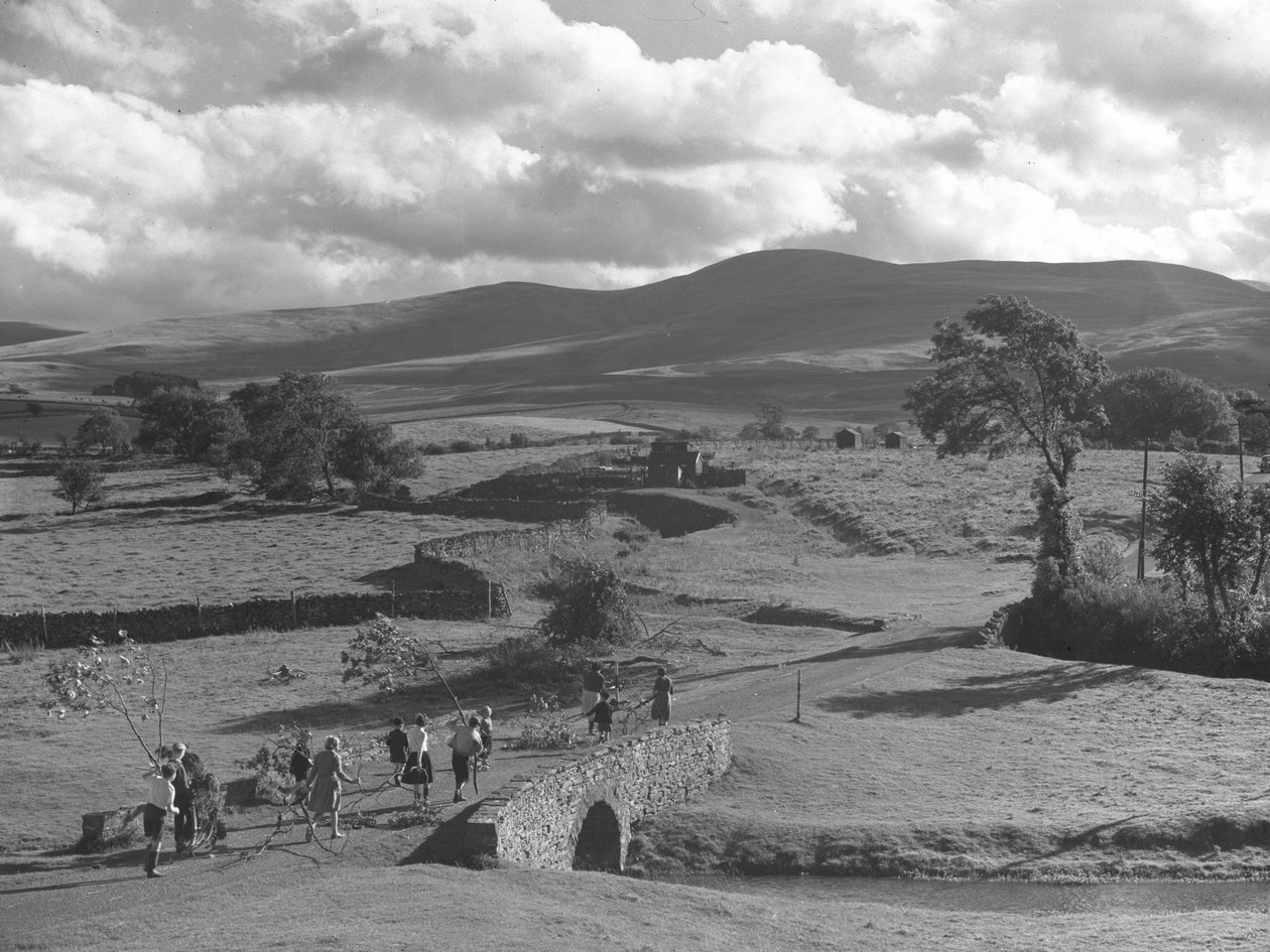 Um grupo de crianças e adultos transporta ramos de árvores por cima de uma ponte para juntar à sua grande pilha, possivelmente uma fogueira de Joseph Hardman