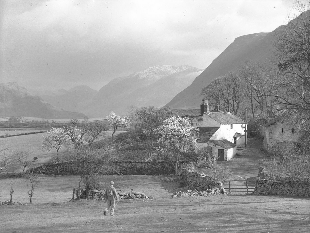 Um homem a caminhar em direção a um caminho e à Casa Gillerthwaite, com o lago e as montanhas em fundo de Joseph Hardman