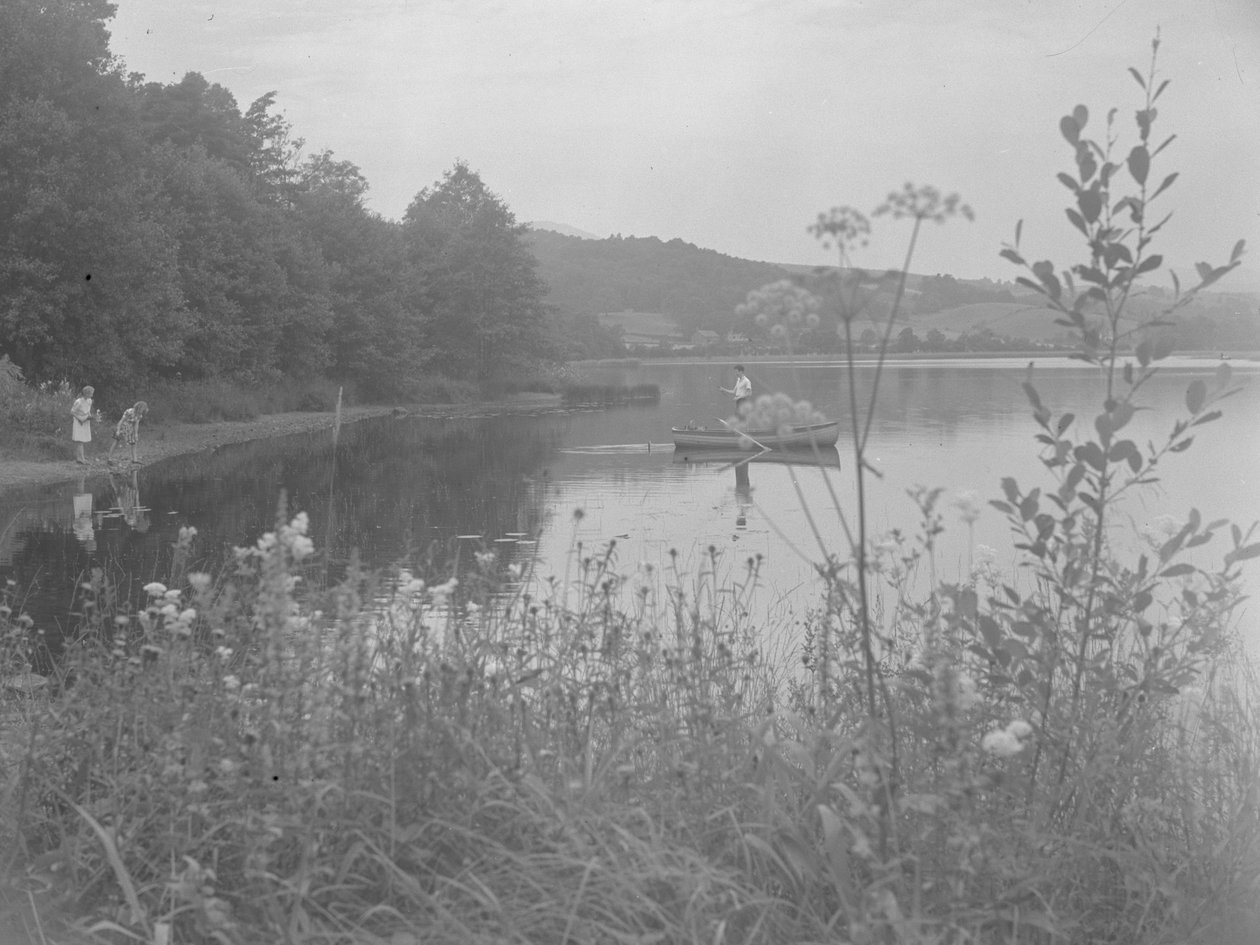 Homem a pescar num barco em Estwaite Water e duas raparigas à beira da água de Joseph Hardman