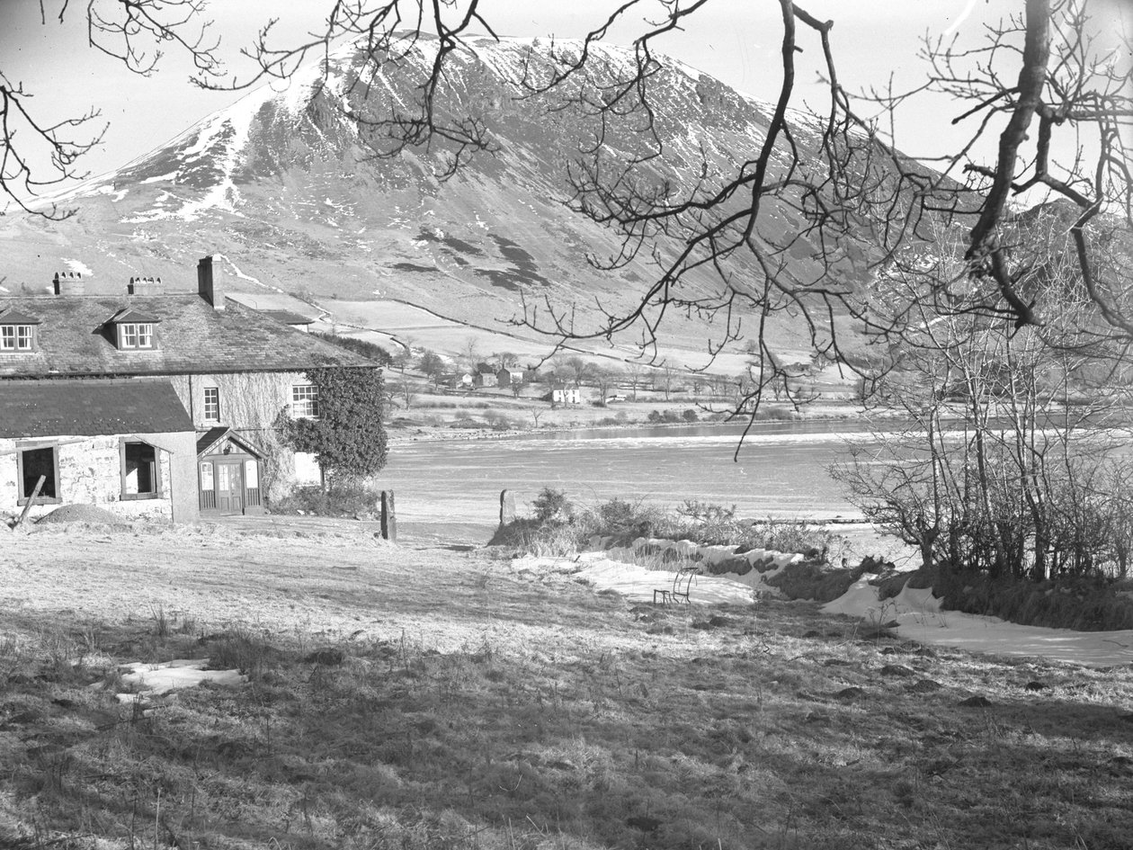 O Anglers Hotel em Ennerdale com árvores em primeiro plano e o lago congelado e as montanhas nevadas mais além de Joseph Hardman