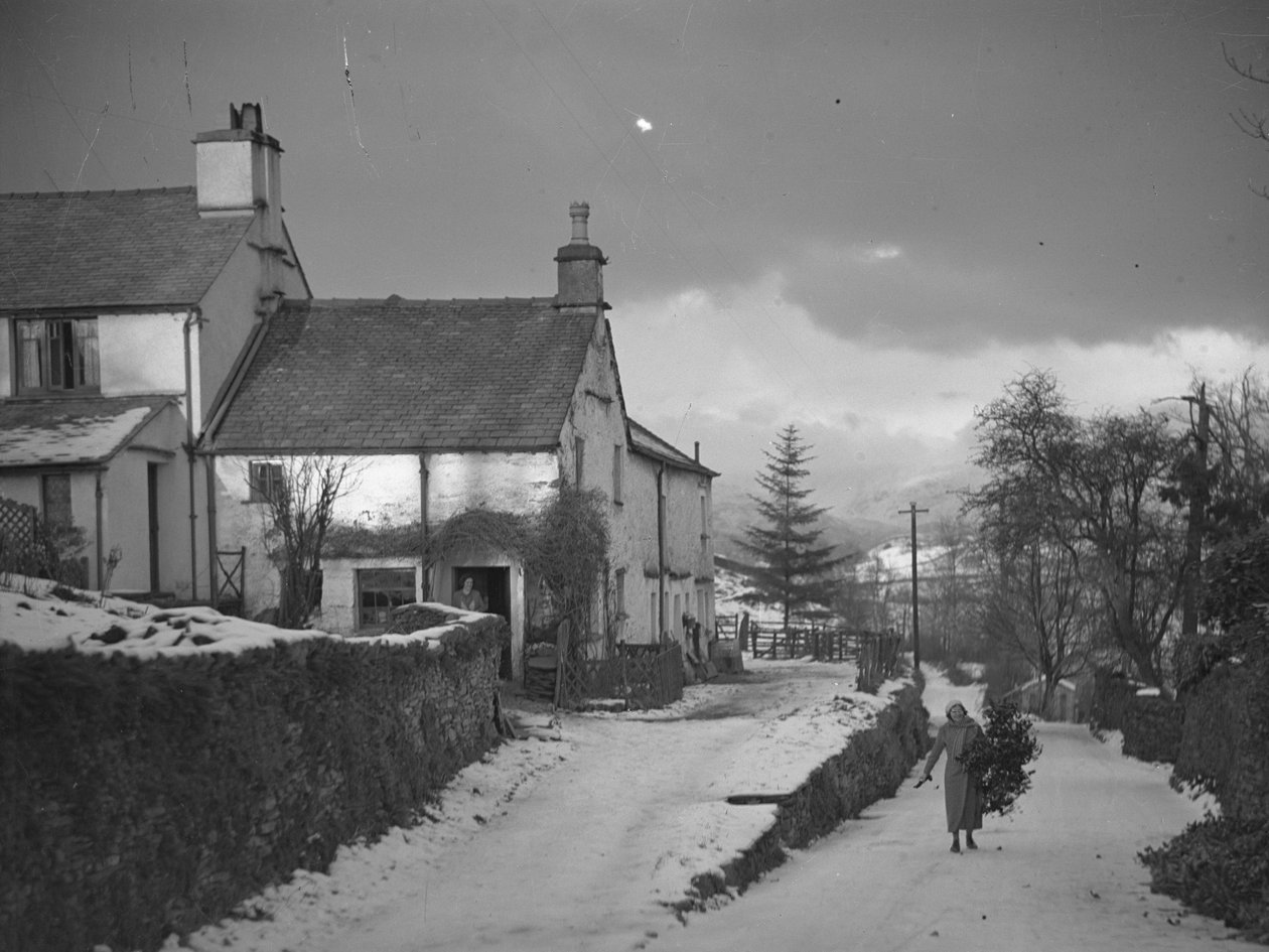 Mulher a carregar um ramo na estrada junto à quinta de Borwick Fold, em Hawkshead, na neve de Joseph Hardman