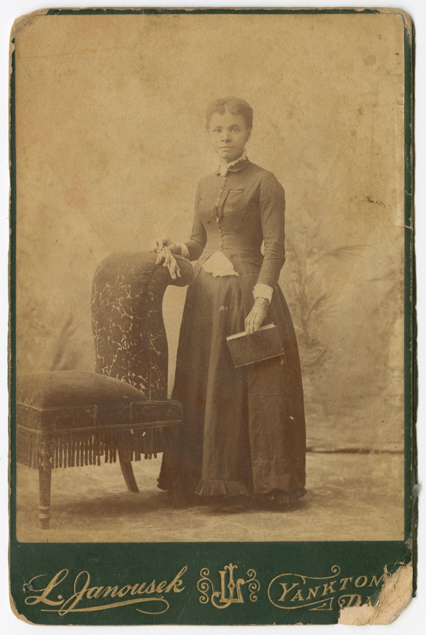 Fotografia de uma mulher de pé ao lado de uma cadeira e segurando um livro, no final do século XIX. de Louis Janousek