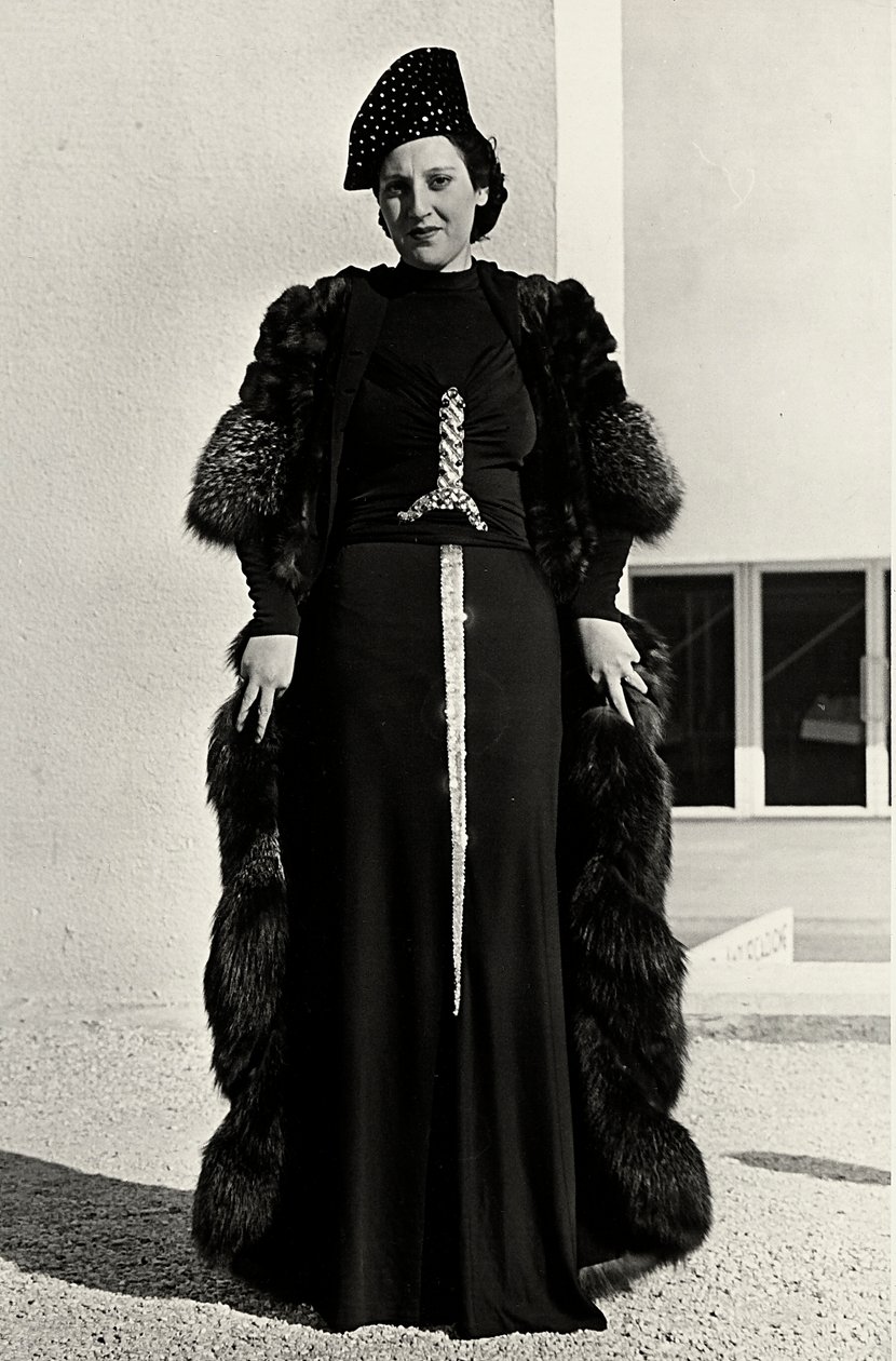 Modelo em vestido de noite criado pela casa de alta costura italiana "Dragoni". A fonte do artigo tem uma decoração de lantejoulas brilhantes em forma de espada. Um chapéu e um sobretudo de pele completam o conjunto. (foto a p/b) de Luis Bogino