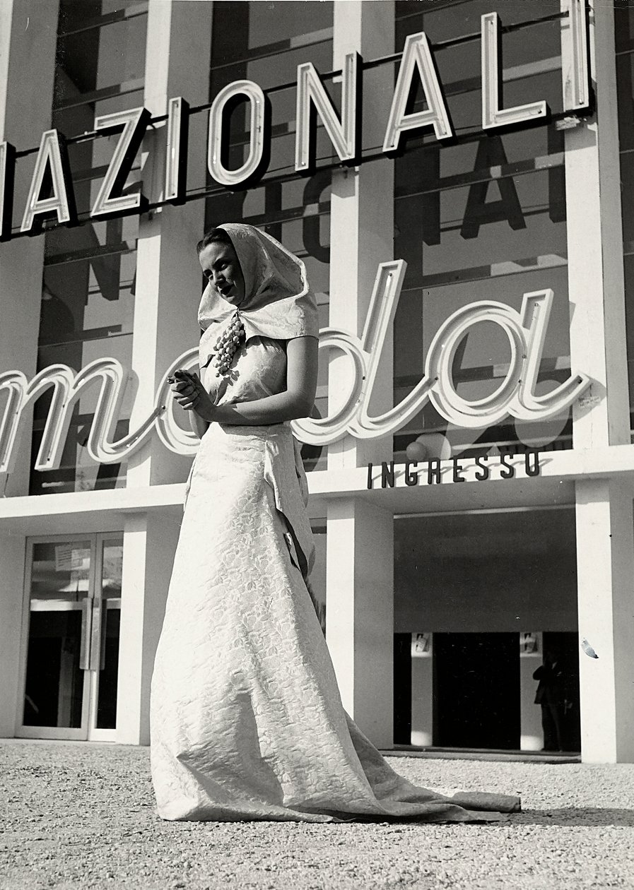 Modelo em vestido de noiva criado pela casa de alta costura "Lamma". O artigo caracteriza-se por um toucado de estilo monástico, segurado no pescoço por um alfinete brilhante na forma de um cacho de uvas. (foto a p/b) de Luis Bogino