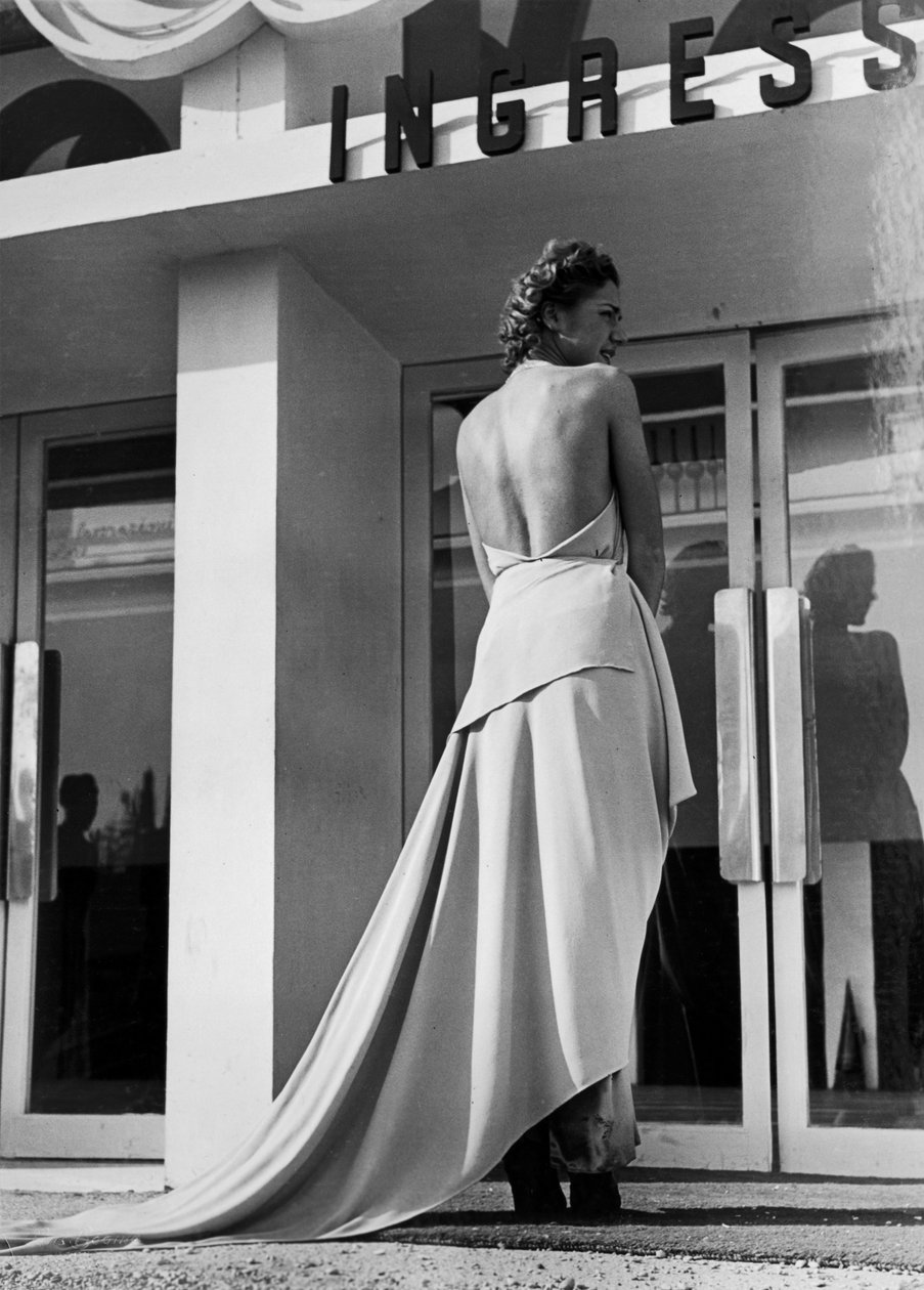 Modelo visto de costas com um vestido de noite criado pela casa de alta costura "Graldi". O artigo é caracterizado por um dorso nu e um trem. (foto a p/b) de Luis Bogino