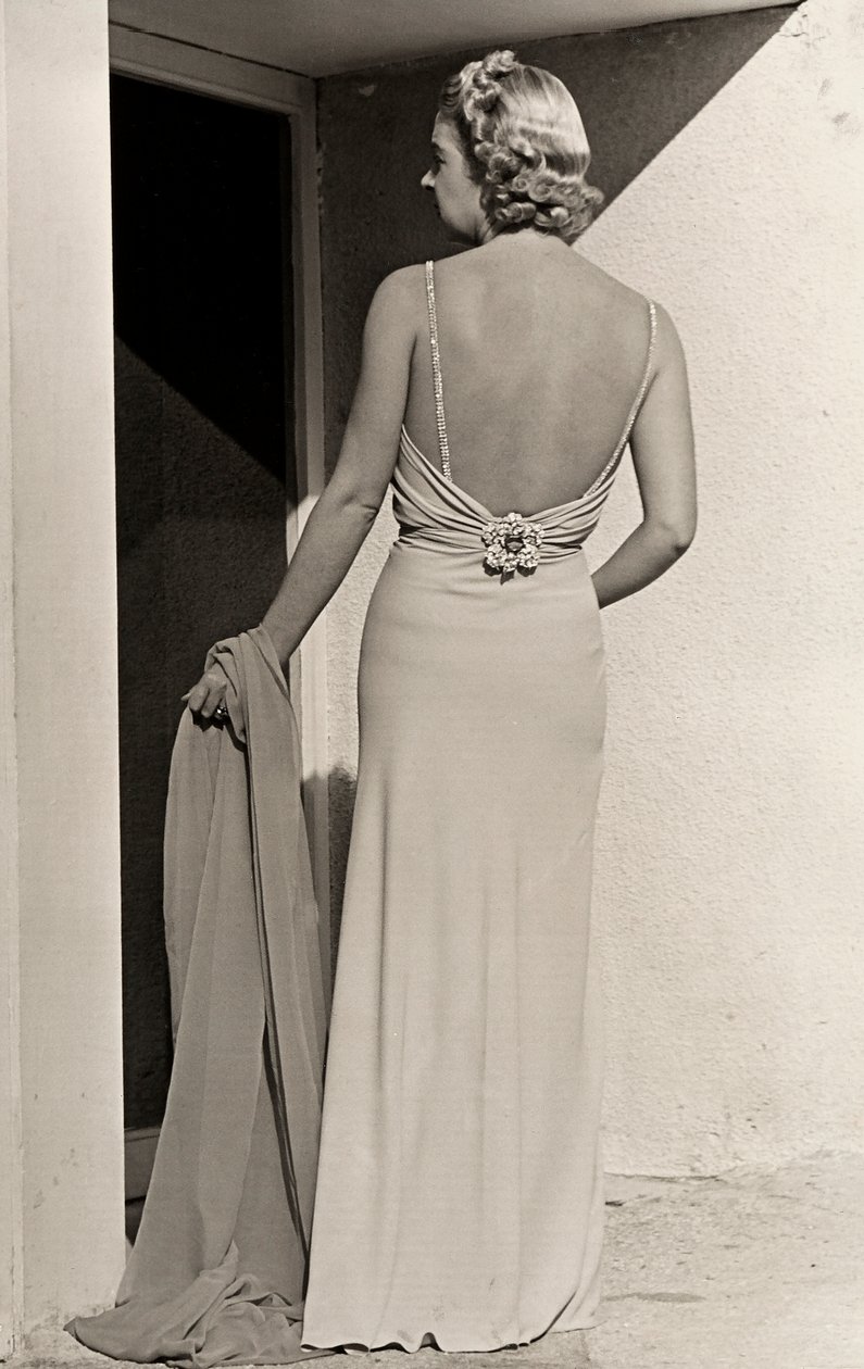 Modelo vista de trás usa vestido de noite da casa de alta costura "Fumach". O artigo deixa as costas nuas e é adornado com um alfinete com jóias. (foto a p/b) de Luis Bogino