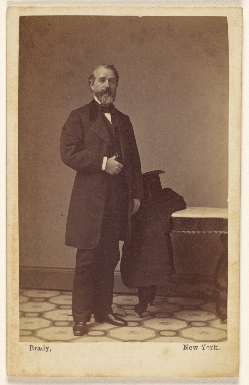 [Homem barbudo não identificado, de pé; com uma cartola e um casaco sobre uma mesa próxima] de Mathew B. Brady