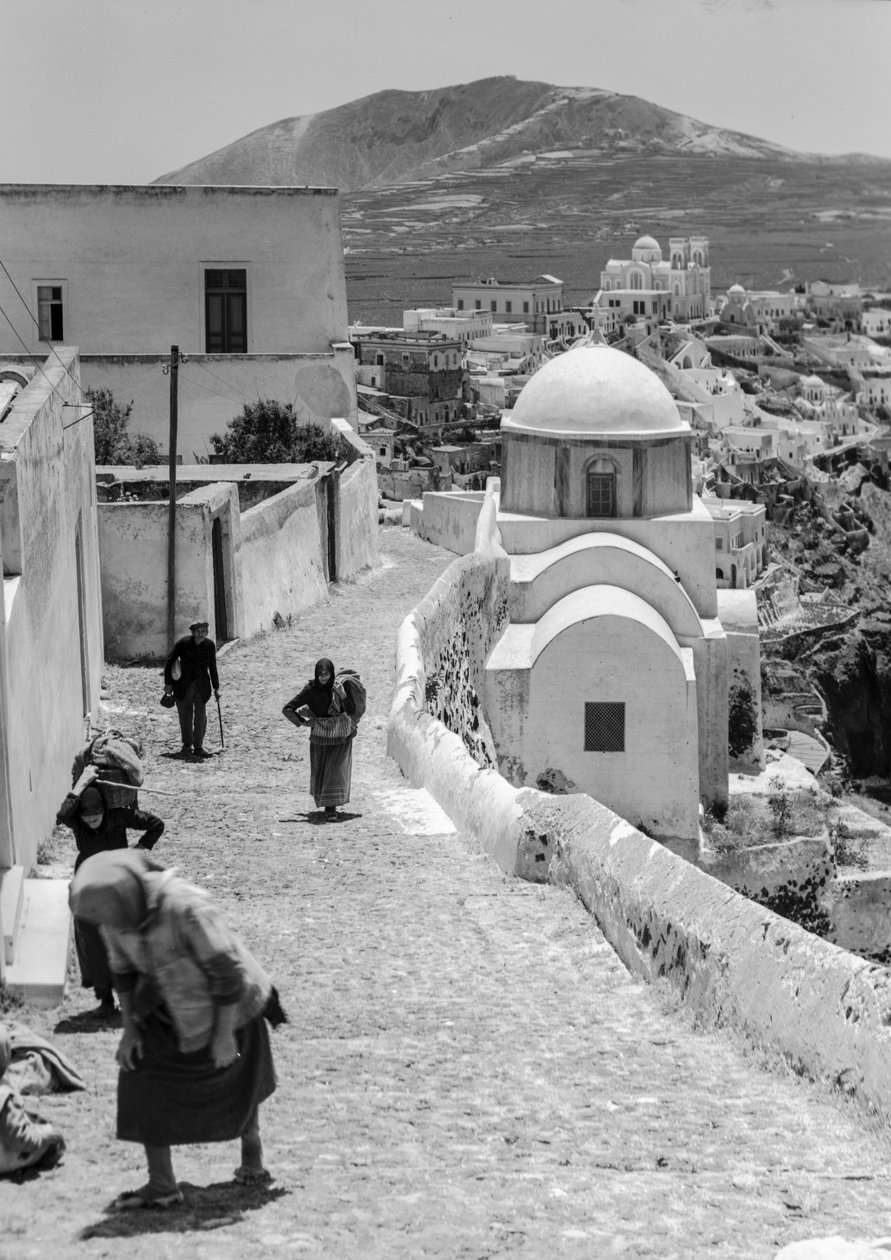 Pessoas de uma aldeia grega caminham por uma estrada de paralelepípedos numa aldeia grega com... de Maynard Owen Williams