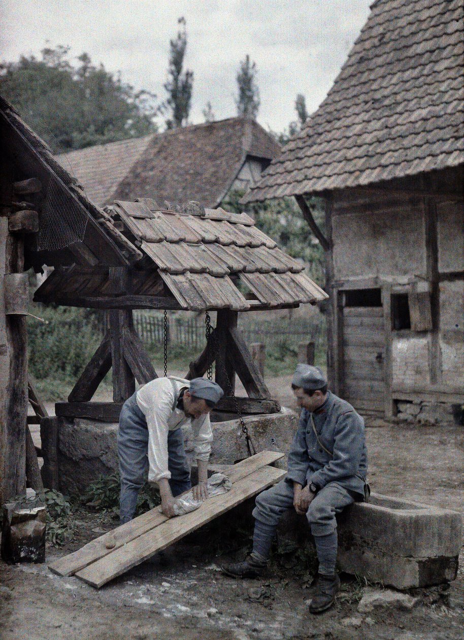 Dois soldados franceses estão cuidando de suas roupas usando tábuas instaladas na calha de uma fonte perto de uma casa de fazenda na cidade de Gildwiller, departamento de Haut-Rhin, Alsácia, França, 21 de junho de 1917 (a de Paul Castelnau