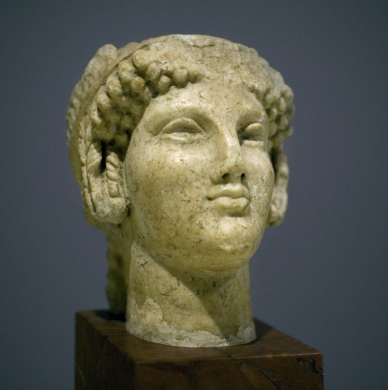 Cabeça de menina (Kore), escultura do período helenístico romano (3o século 2 depois da nossa era), rosto muito expressivo, maçãs do rosto proeminentes a leste, sorriso, cabelo encaracolado, estilo arcaico de Ionie no século 6 antes da nossa era que se per de Roman