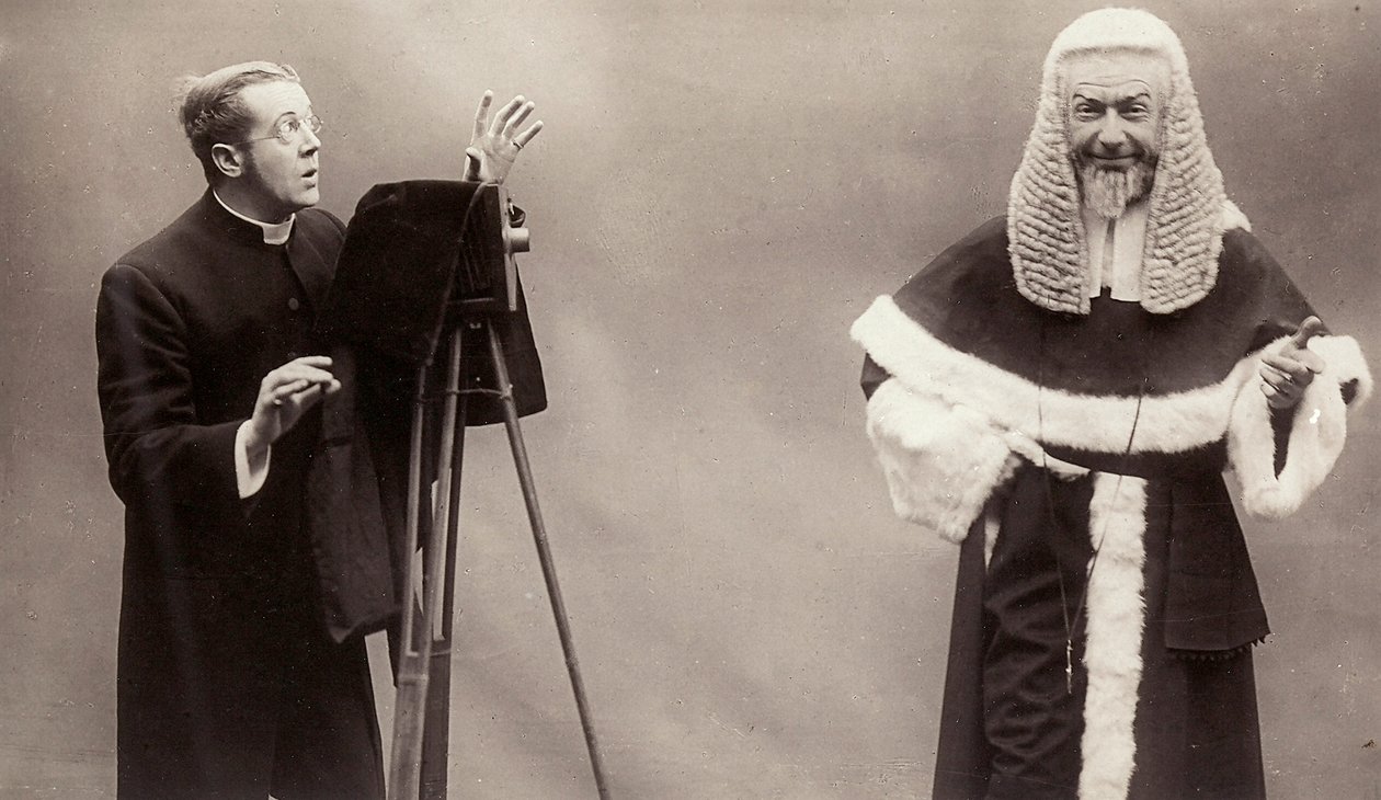 Um homem de batina aponta a lente da sua câmara a um homem vestido como um papa. de Rotary Photographic Co Ltd