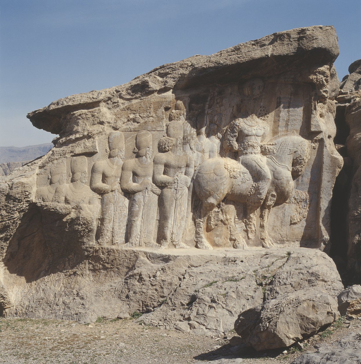 Relevo de rocha representando Shapur I (241-72 dC) e sua família usando emblemas heráldicos em seus chapéus, com uma inscrição em três línguas no cavalo em grego, parta e persa médio. de Sasanian