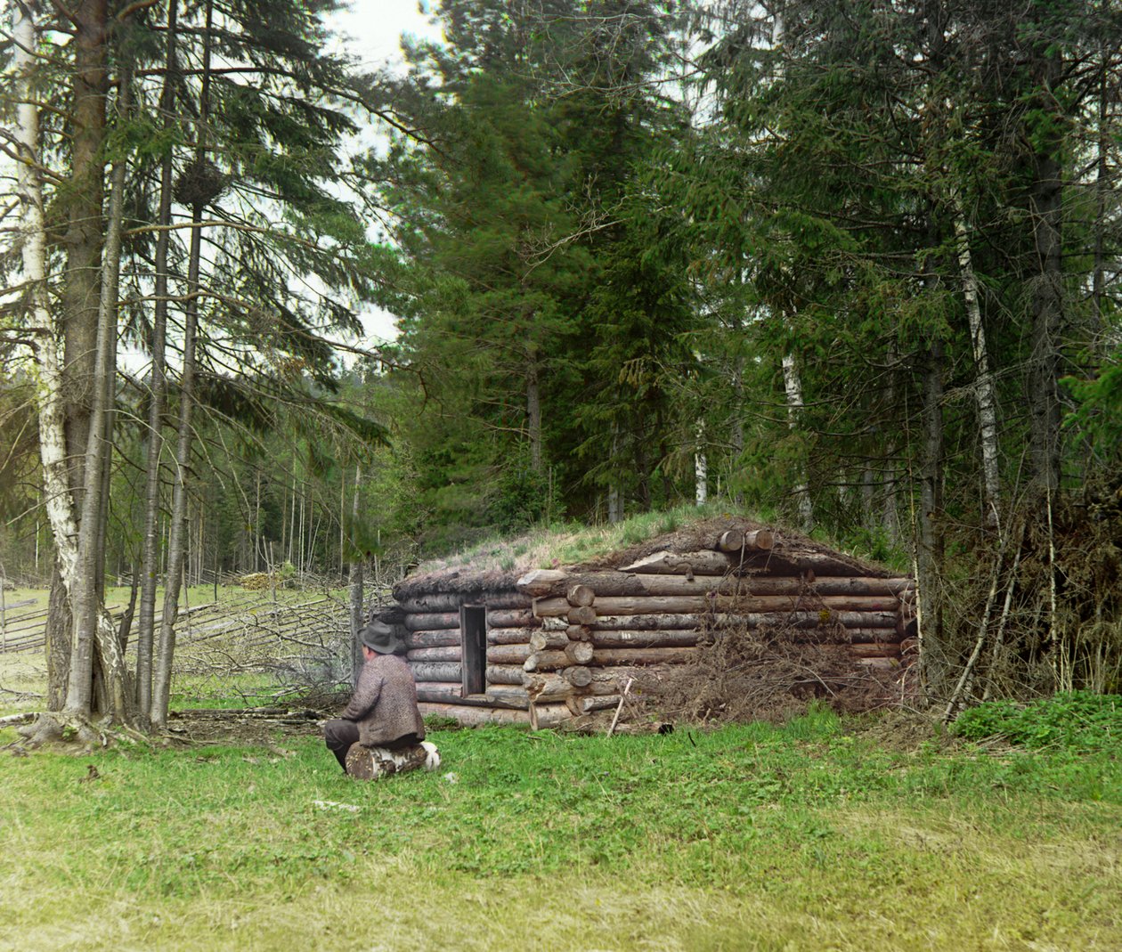 Um homem na frente de uma cabana para lenhadores e kuria (queima de carvão) na floresta, Império Russo, entre 1905 e 1915 de Sergey Prokudin Gorsky