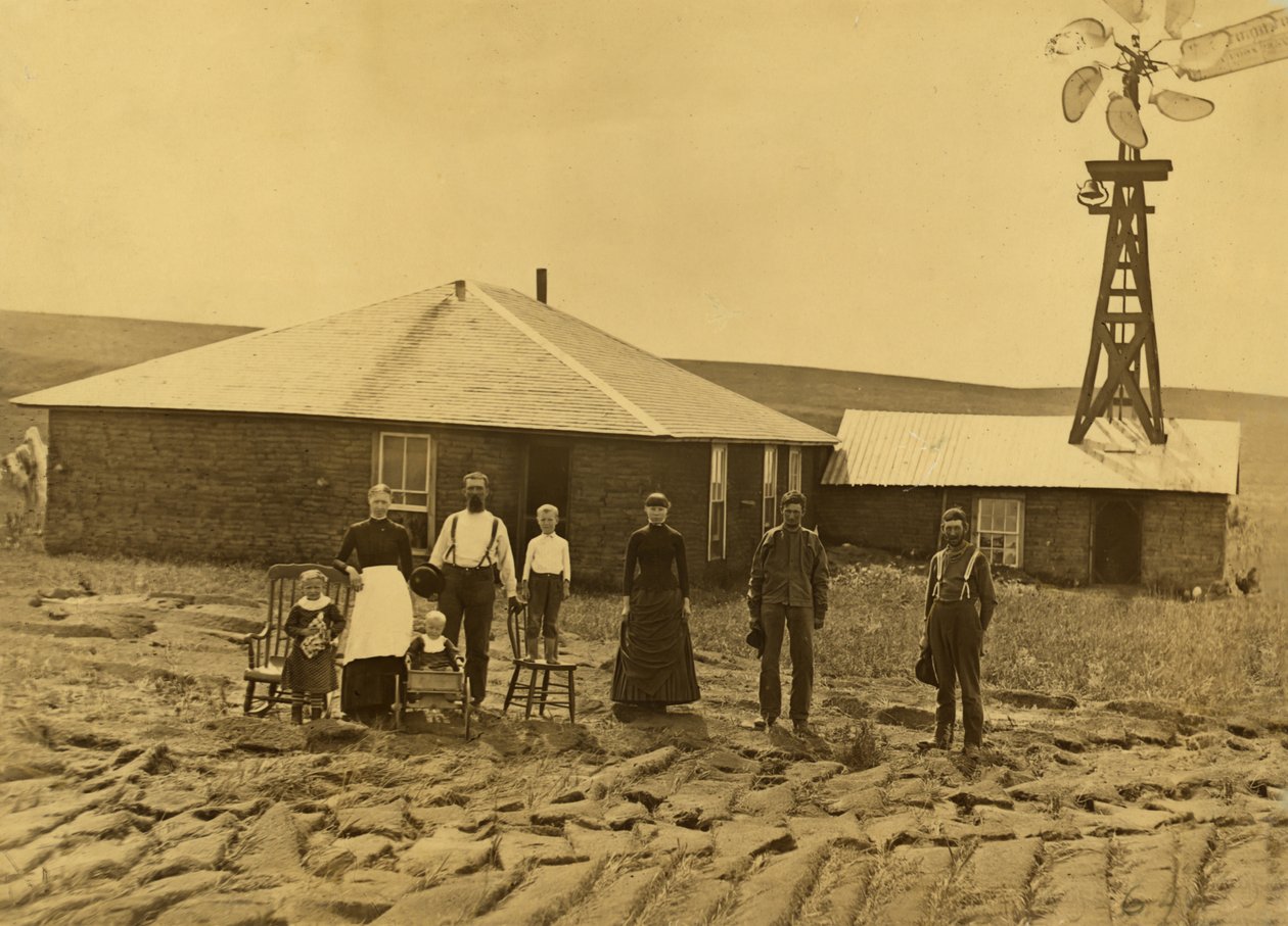 Família de colonos, no exterior da sua casa de relva com um moinho de vento no telhado do edifício adjacente no condado de Custer, Nebraska, c.1885 (fotografia a preto e branco) de Solomon D. Butcher